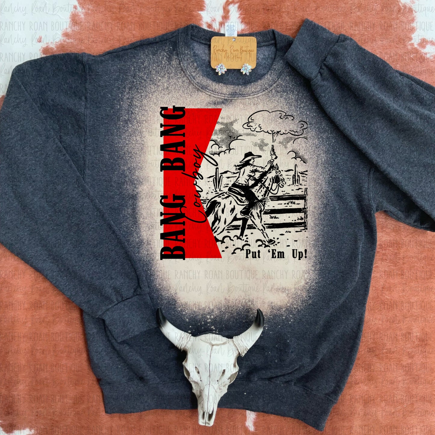 Unisex crew sweatshirt featuring a graphic of a cowboy with the text “Bang Bang Cowboy” and “Put ’Em Up,” designed with a bleach splatter pattern.