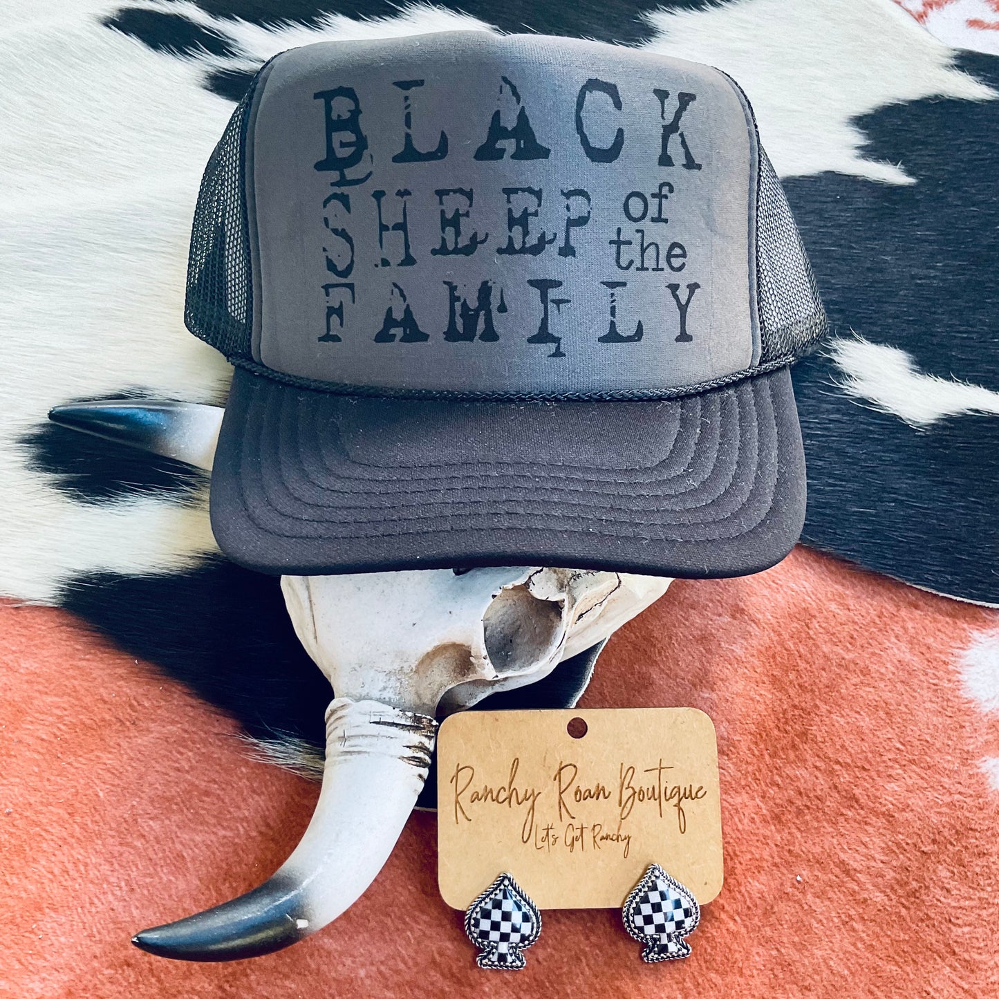 “Black Sheep of the Family” trucker hat displayed on a cow skull with a Western theme, highlighting its bold text and adjustable snapback.