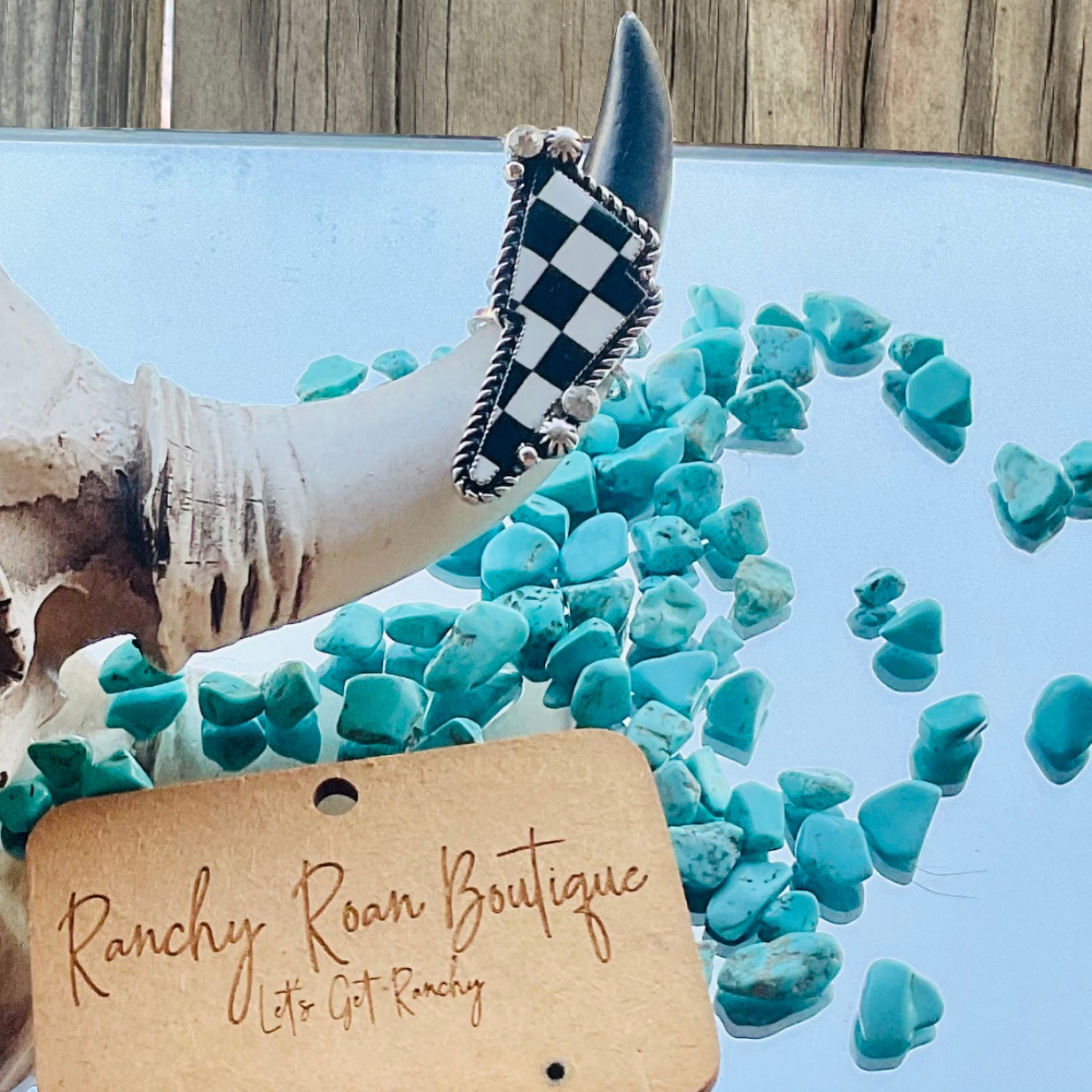 Close-up of the checker pattern thunder cuff ring resting on a horn, surrounded by turquoise stones, highlighting the ring’s unique checkerboard design.