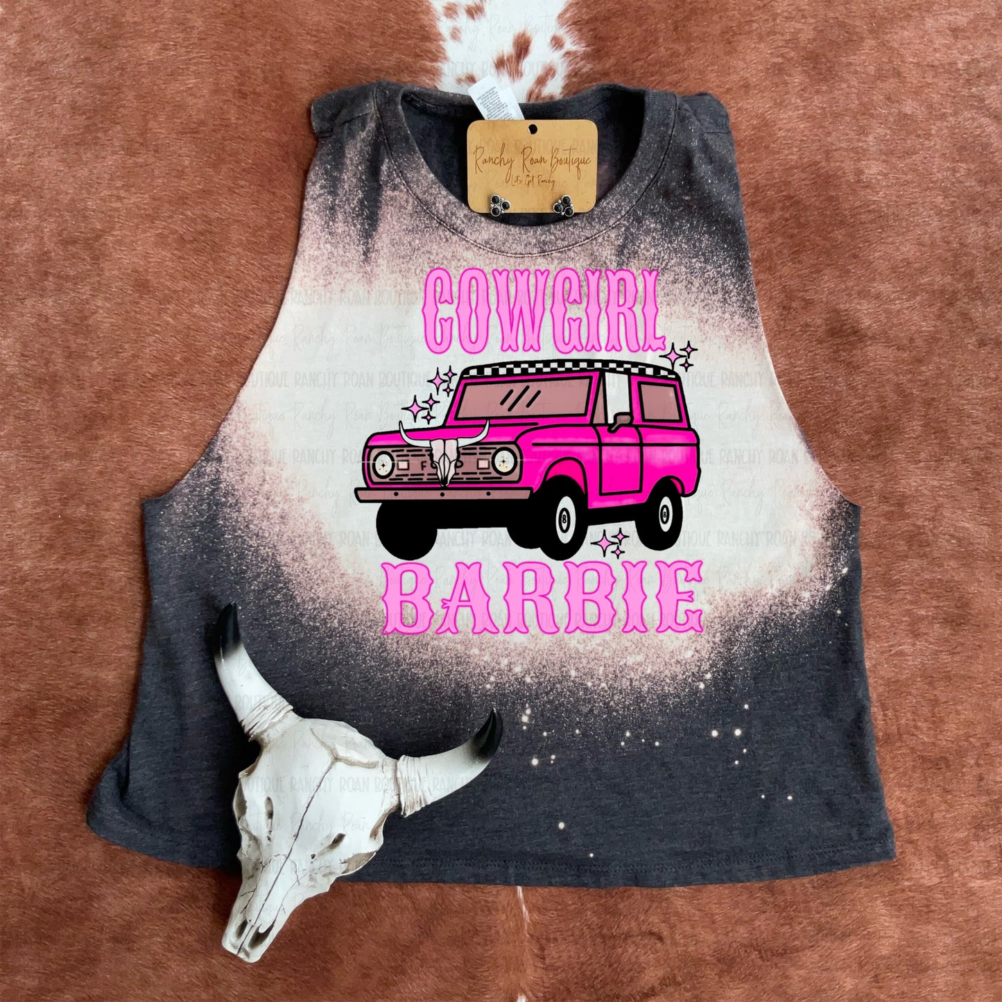 Western-inspired bleached crop top featuring a pink Bronco design, displayed on cowhide background.