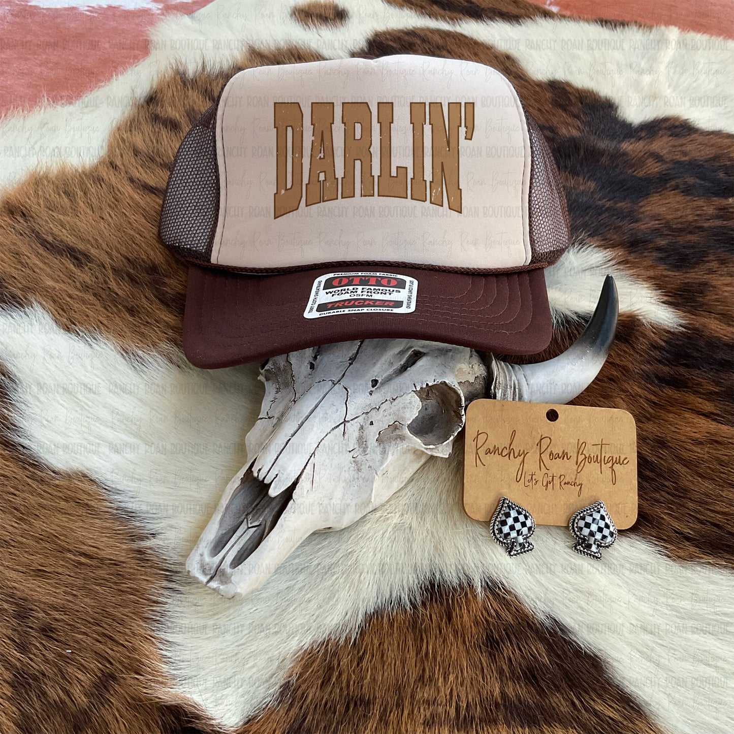 Brown and tan DARLIN’ trucker hat with mesh back displayed on cowhide with Western skull – Ranchy Roan Boutique”