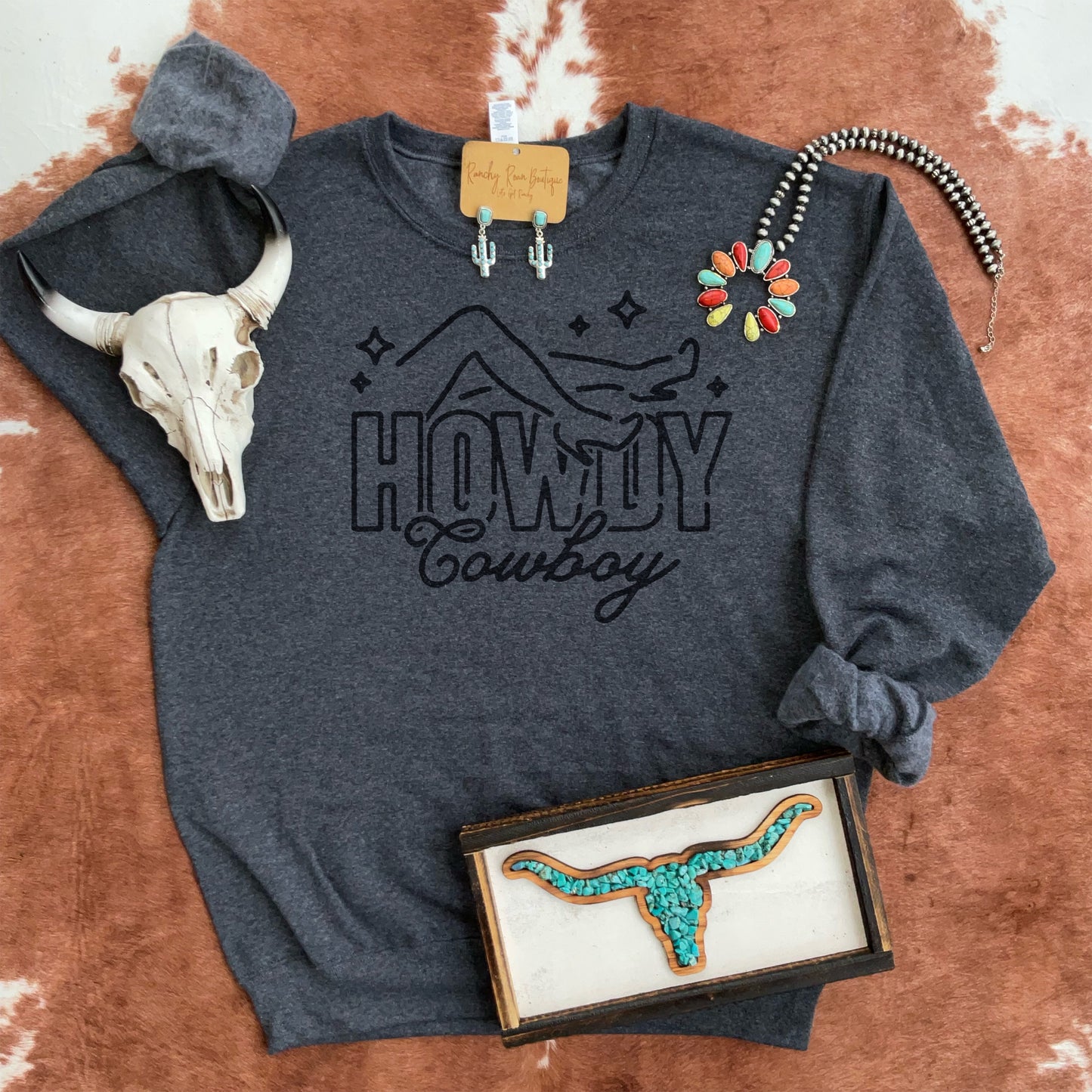 Howdy Cowboy graphic sweatshirt styled with turquoise jewelry and a rustic skull, perfect for Western boutiques.