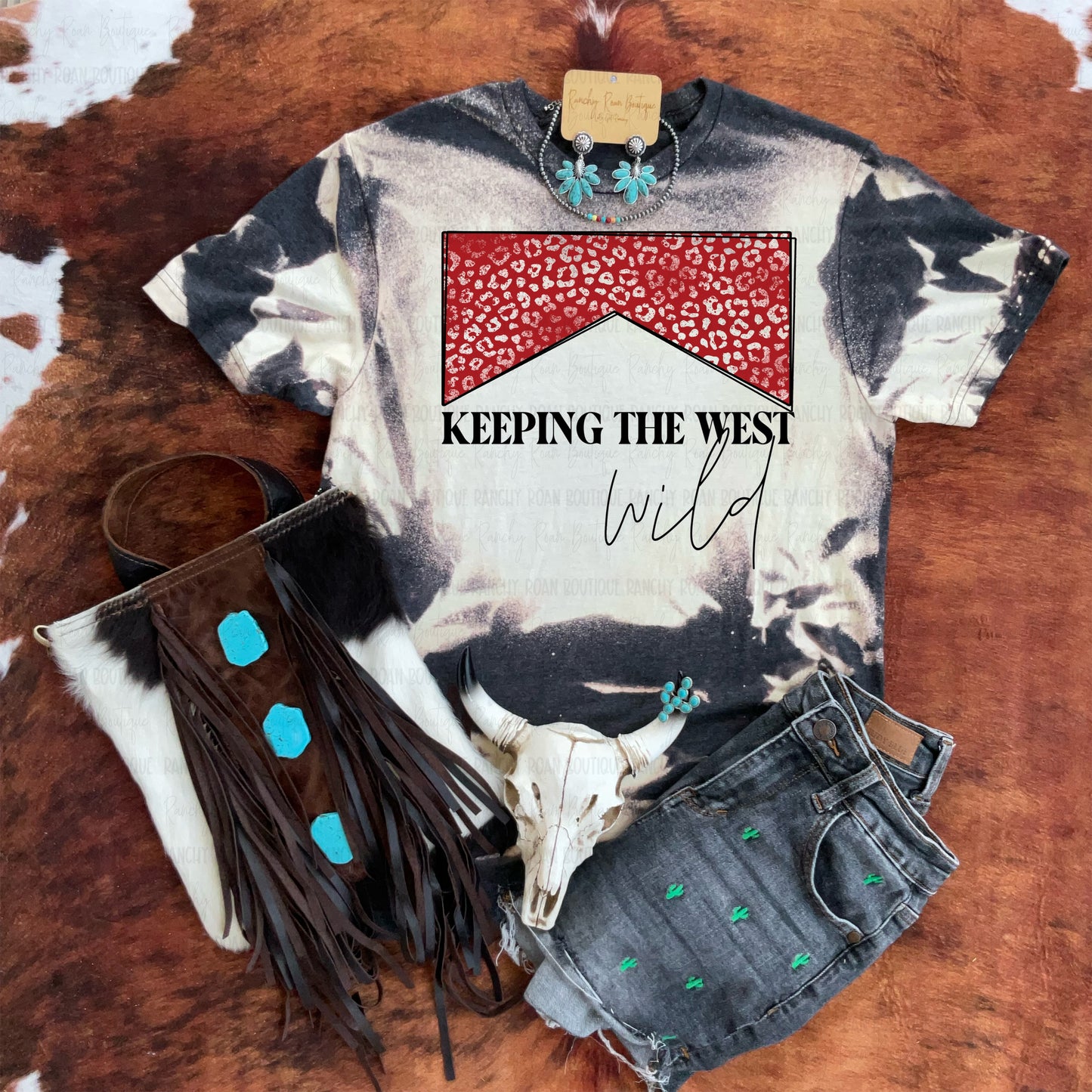 Western bleached graphic tee with red leopard yoke design, styled with denim and turquoise jewelry on a cowhide background.