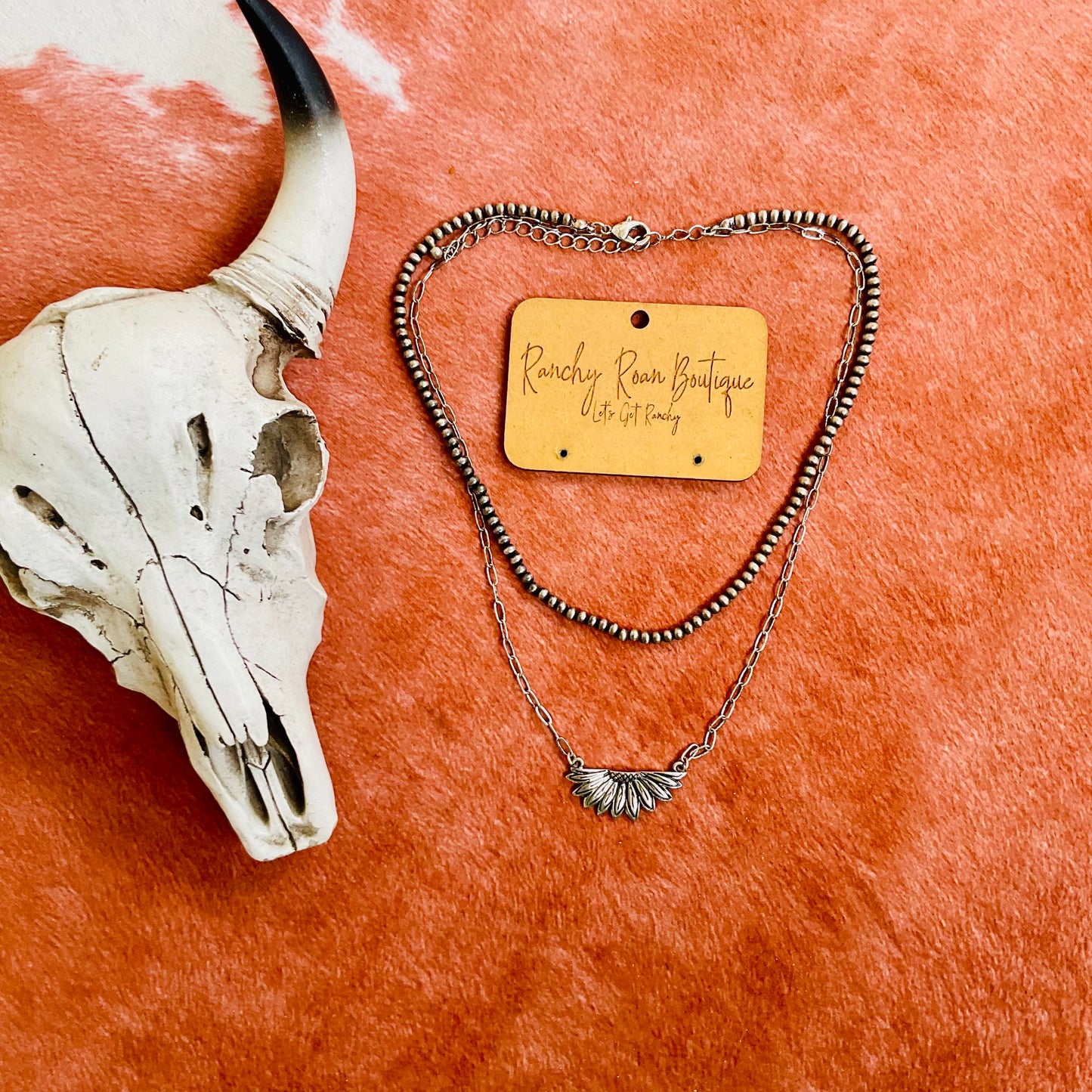 Stylish burnished silver-tone necklace featuring sunflower casting and layered design, placed on a Western cowhide for a rustic aesthetic.