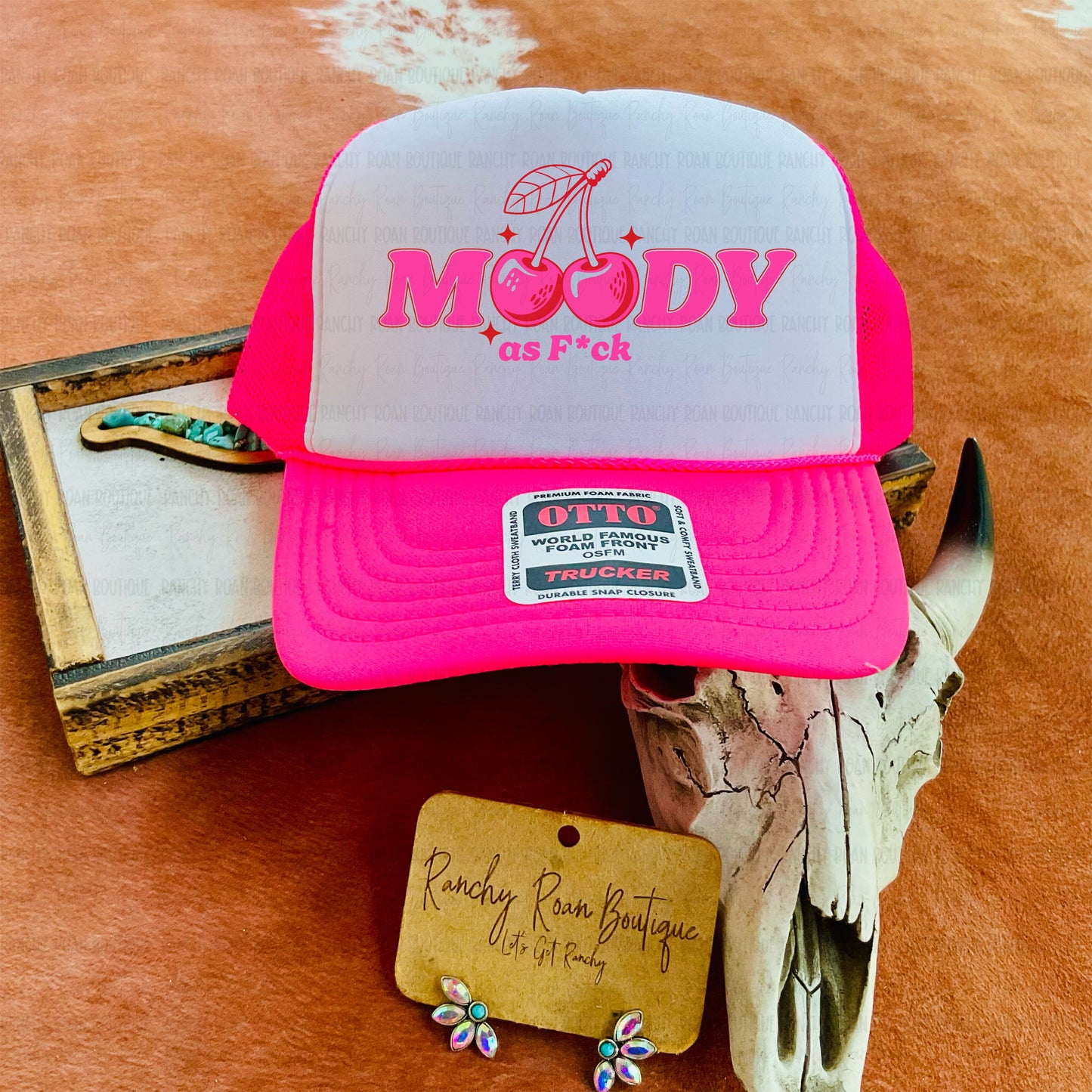 Hot pink foam trucker hat featuring a “Moody as Fck” sublimation design with cherries, breathable mesh back, and adjustable snapback.
