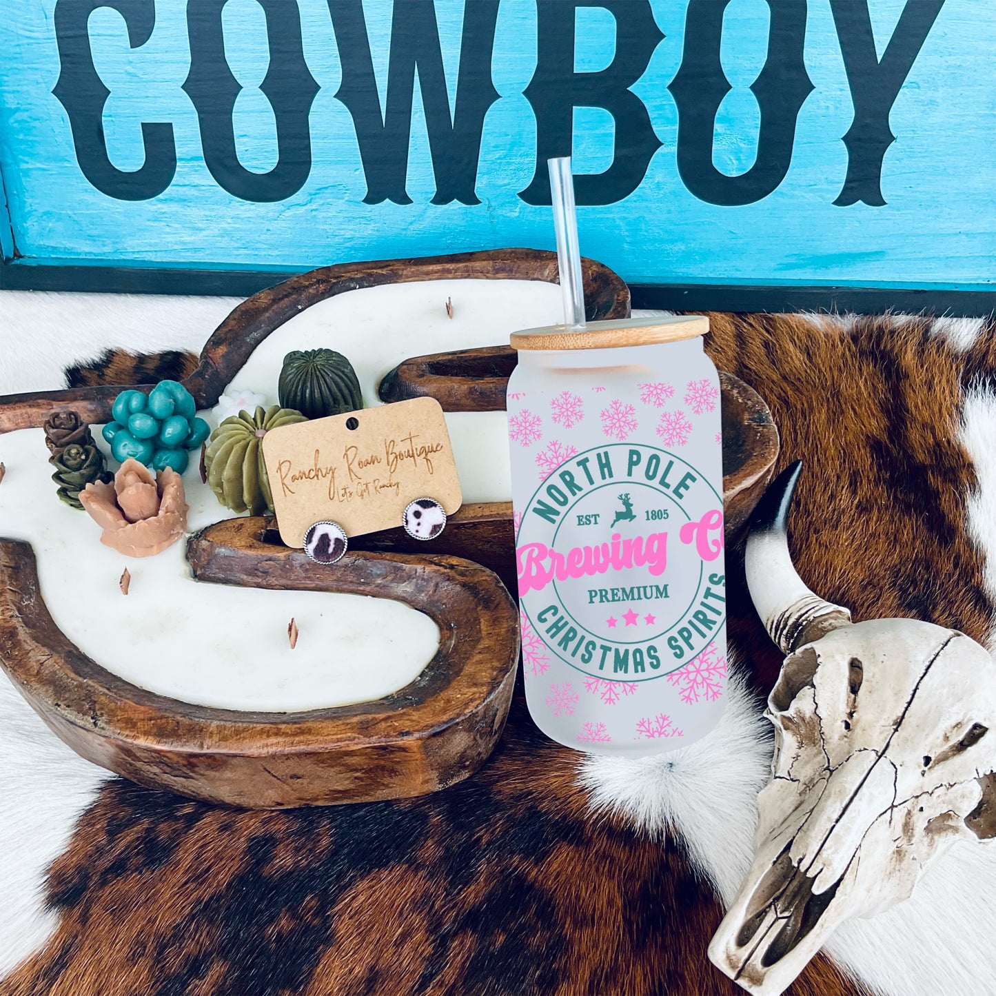 North Pole Brewing Co. Frosted Glass Tumbler with bamboo lid and straw, displayed on a Western-themed setup featuring cowhide and rustic decor.