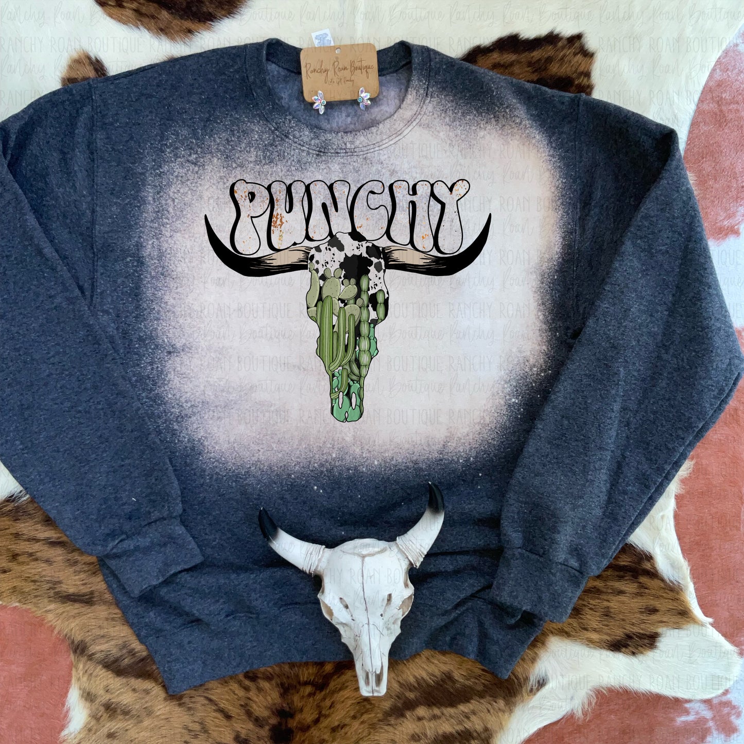 Western sweatshirt featuring a sublimation “Punchy” design with a cow skull and cactus, bleach-dyed details, and a unisex fit.