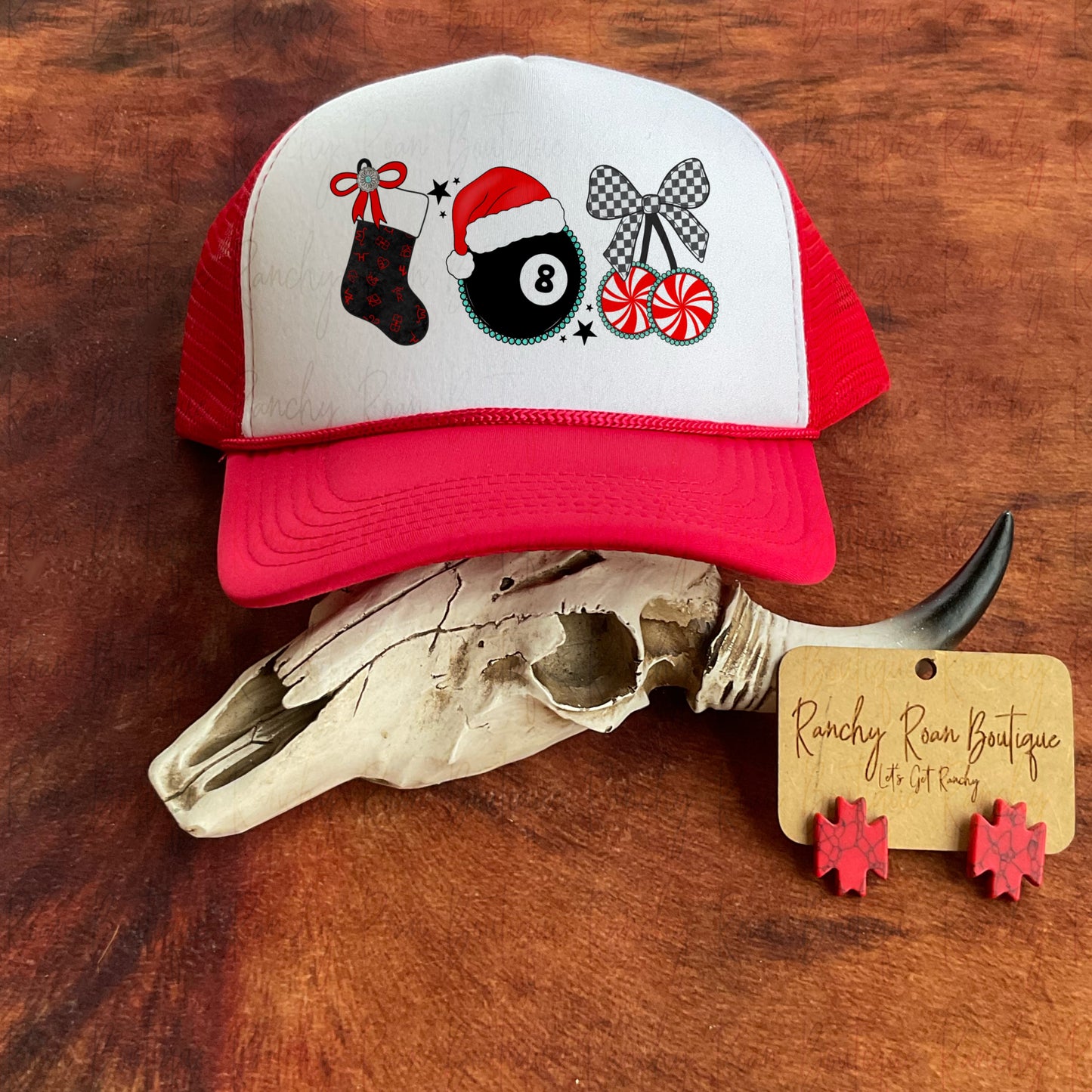 Trucker hat featuring a festive Western Christmas design with a stocking, Santa hat, and candy graphics, displayed with cow skull decor.