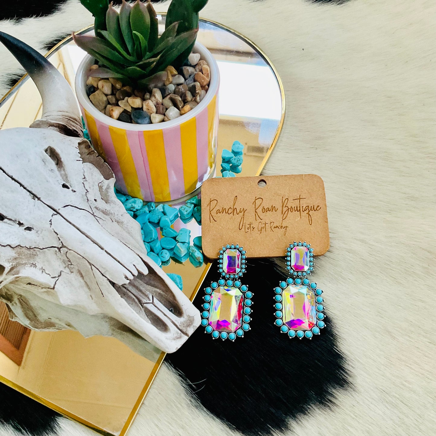 Pair of Western octagon stud earrings featuring burnished silver and turquoise accents with a bold AB stone, displayed alongside a succulent and cow skull decor.