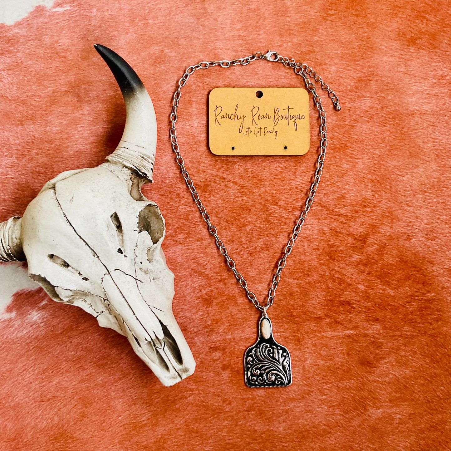 Western cow tag pendant necklace with engraved scrollwork, hanging from an adjustable silver chain, perfect for rodeo and ranch-inspired fashion.