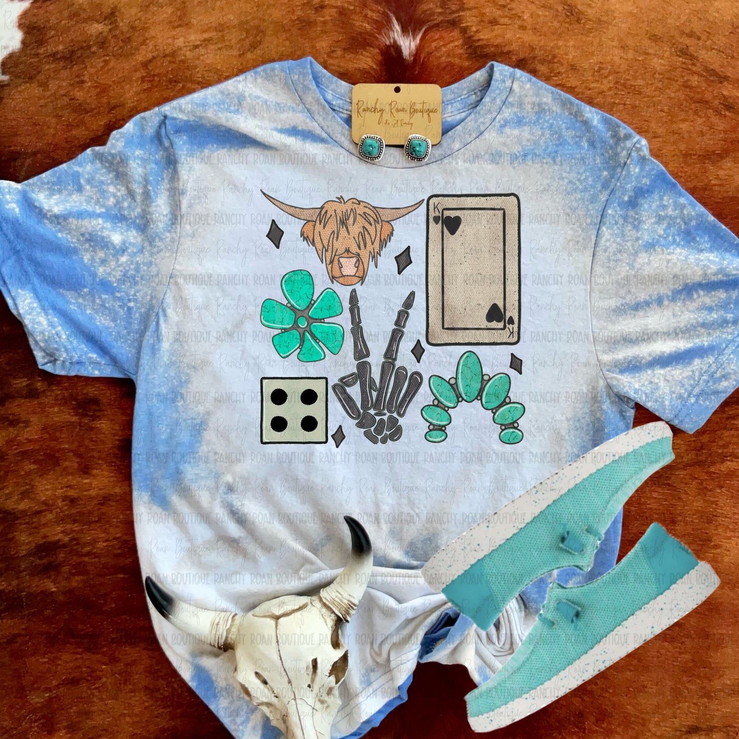 Western bleach tee with sublimated collage of cow skull, turquoise conchos, skeleton hands, dice, cards, and Highland cow, styled with turquoise shoes
