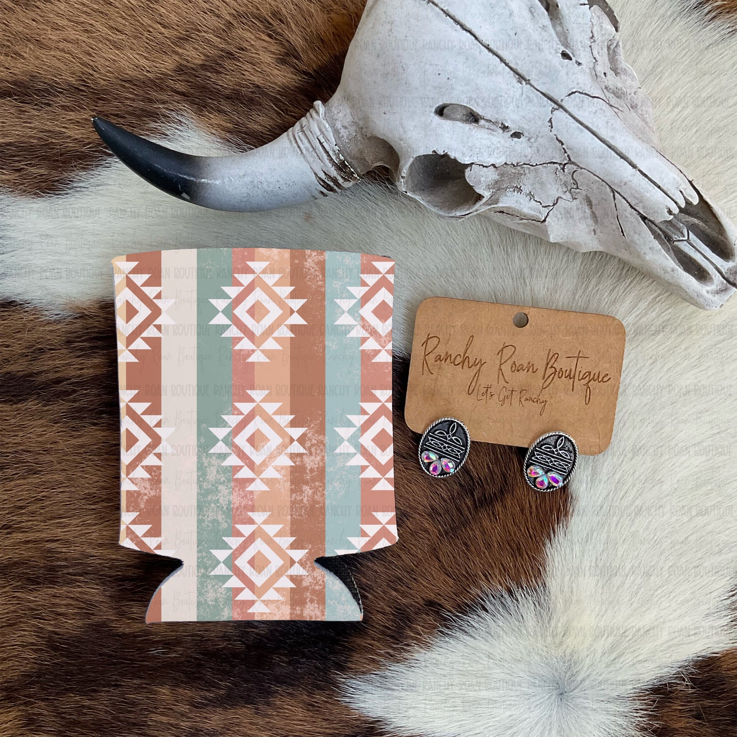 Western Aztec sublimated koozie in rust, sage, and cream pattern, styled with skull and earrings on cowhide