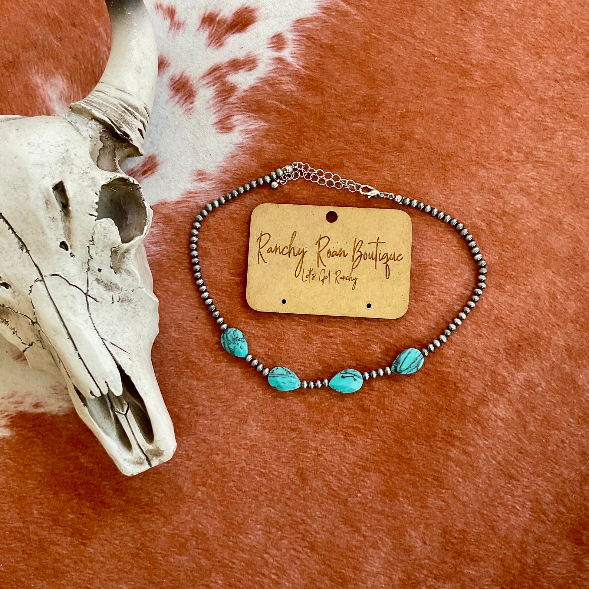 Close-up of a Navajo-style pearl choker featuring turquoise stones, styled with a Western cow skull against a cowhide backdrop.
