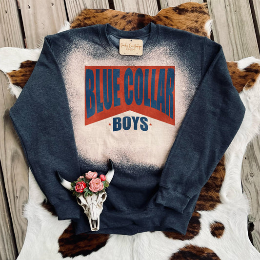 Blue Collar Boys Distressed Western Sweatshirt with bold red and blue text on a charcoal bleached background, lying on a cowhide rug.