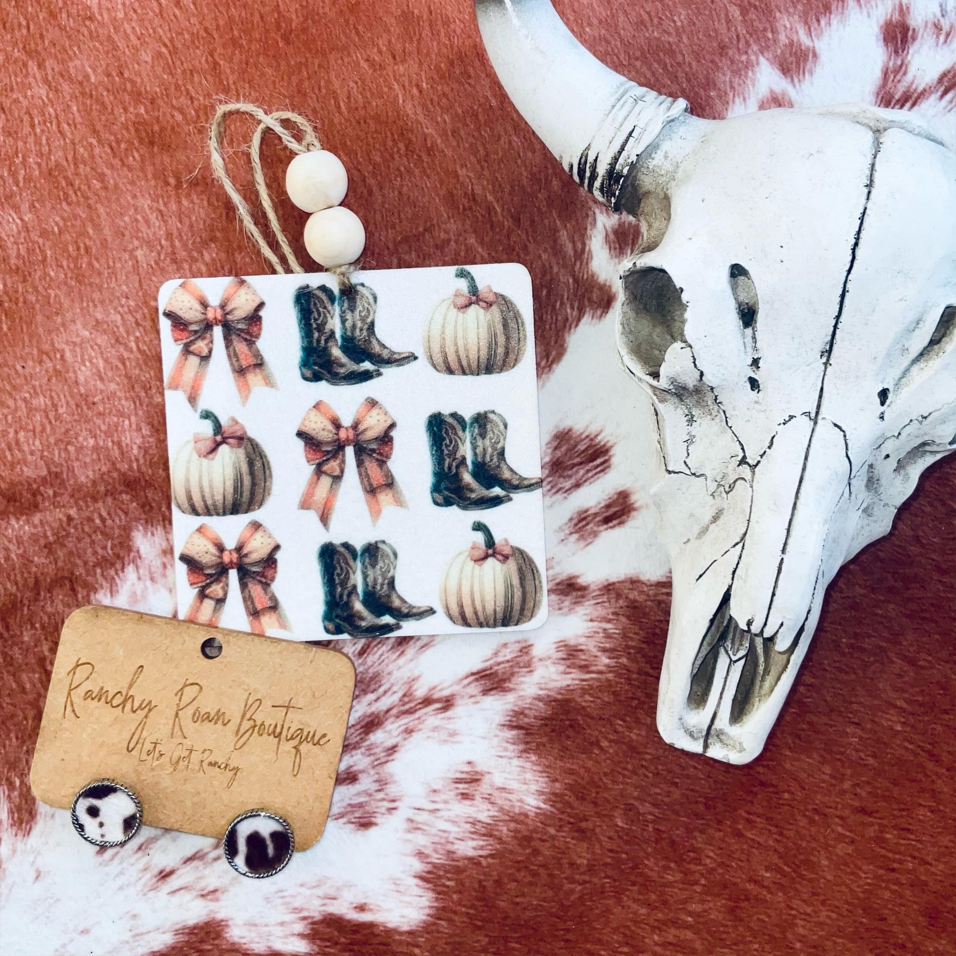 A square felt freshie showcasing a pattern of cowboy boots, bows, and pumpkins, with wooden beads.