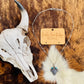 Western Checker Cow Head Necklace styled with a Western skull prop, showcasing its adjustable chain and unique checker-patterned cow head design.