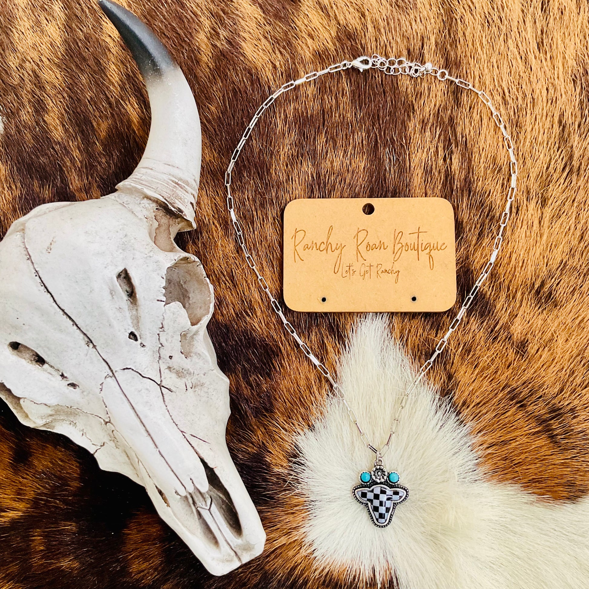 Western Checker Cow Head Necklace styled with a Western skull prop, showcasing its adjustable chain and unique checker-patterned cow head design.
