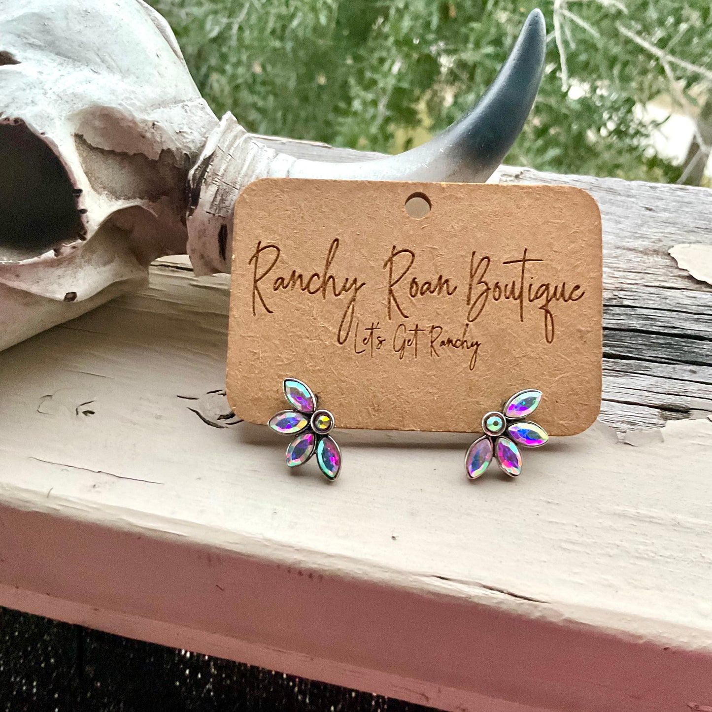 Close-up of iridescent floral stud earrings on Ranchy Roan Boutique card, highlighting the light-reflecting stones and Western vibe.