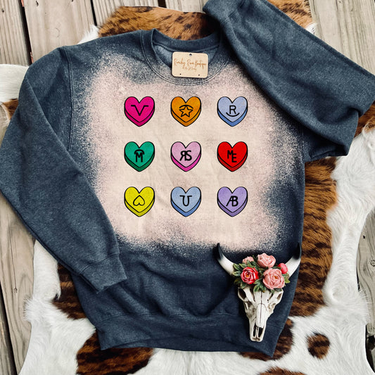  A fun sweatshirt featuring colorful candy-heart designs with Western icons, displayed with a cowhide backdrop.