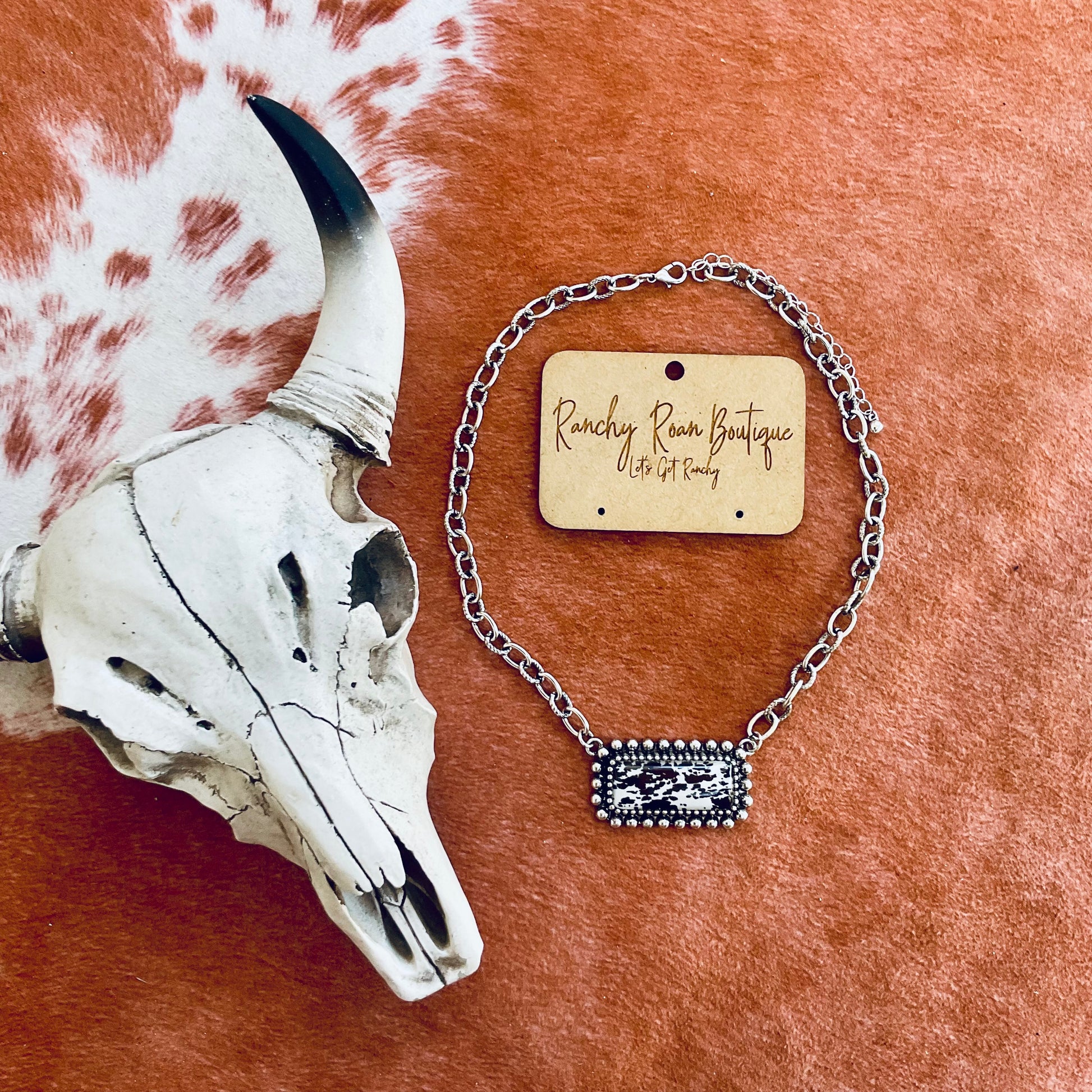 Cow Printed Bar Necklace - Western Cowhide Style Displayed on a rustic background with a cow skull accent 