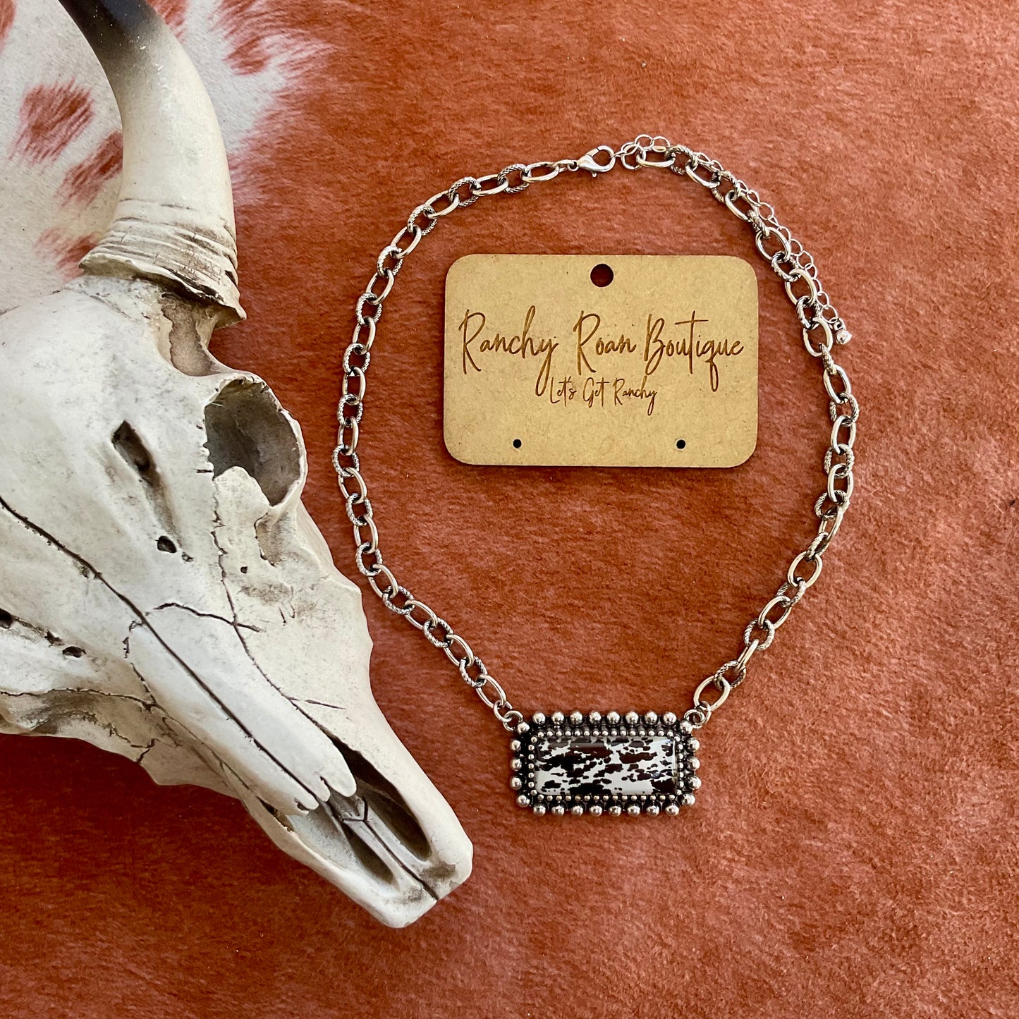 Cow Printed Bar Necklace - Western Cowhide Style Displayed on a rustic background with a cow skull accent Close up