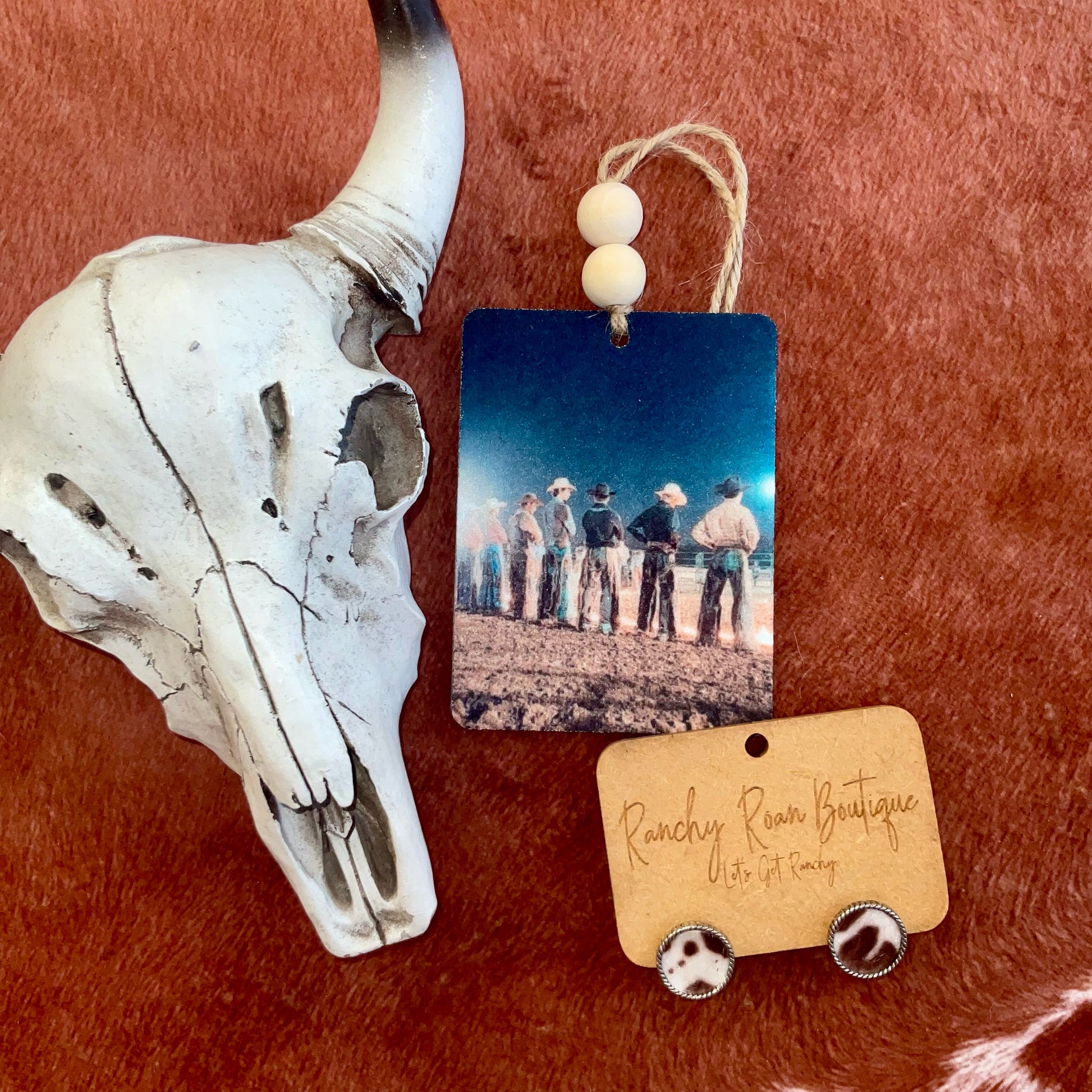 A rectangular felt freshie showing a group of cowboys standing at sunset, with wooden beads and a rustic background.