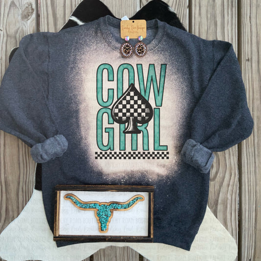 Dark heather sweatshirt with a teal “Cowgirl” design and checkered spade graphic, styled with Western decor.