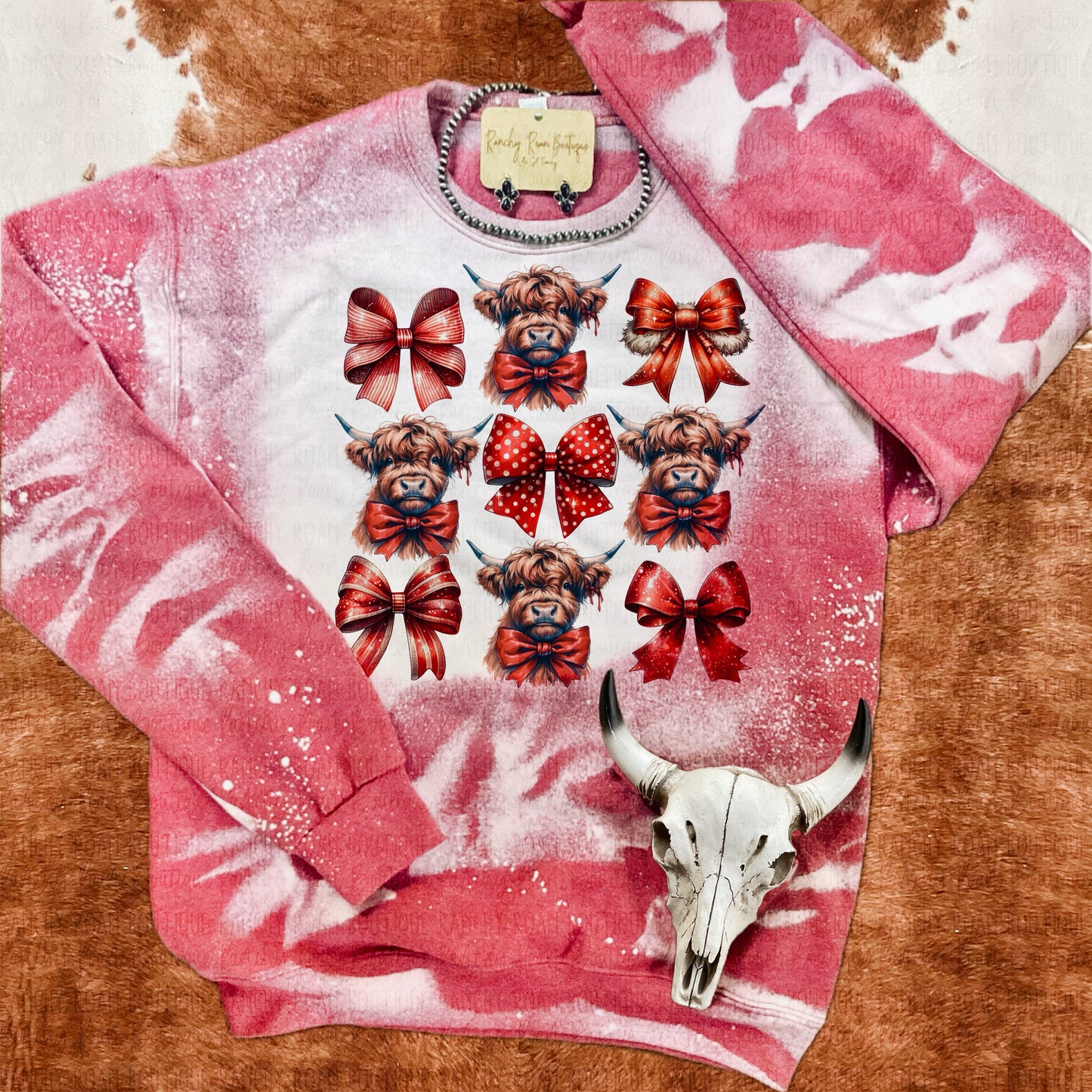 Vintage red bleached sweatshirt featuring multiple highland cow graphics with red and polka dot bows, displayed with a decorative skull on a cowhide background.