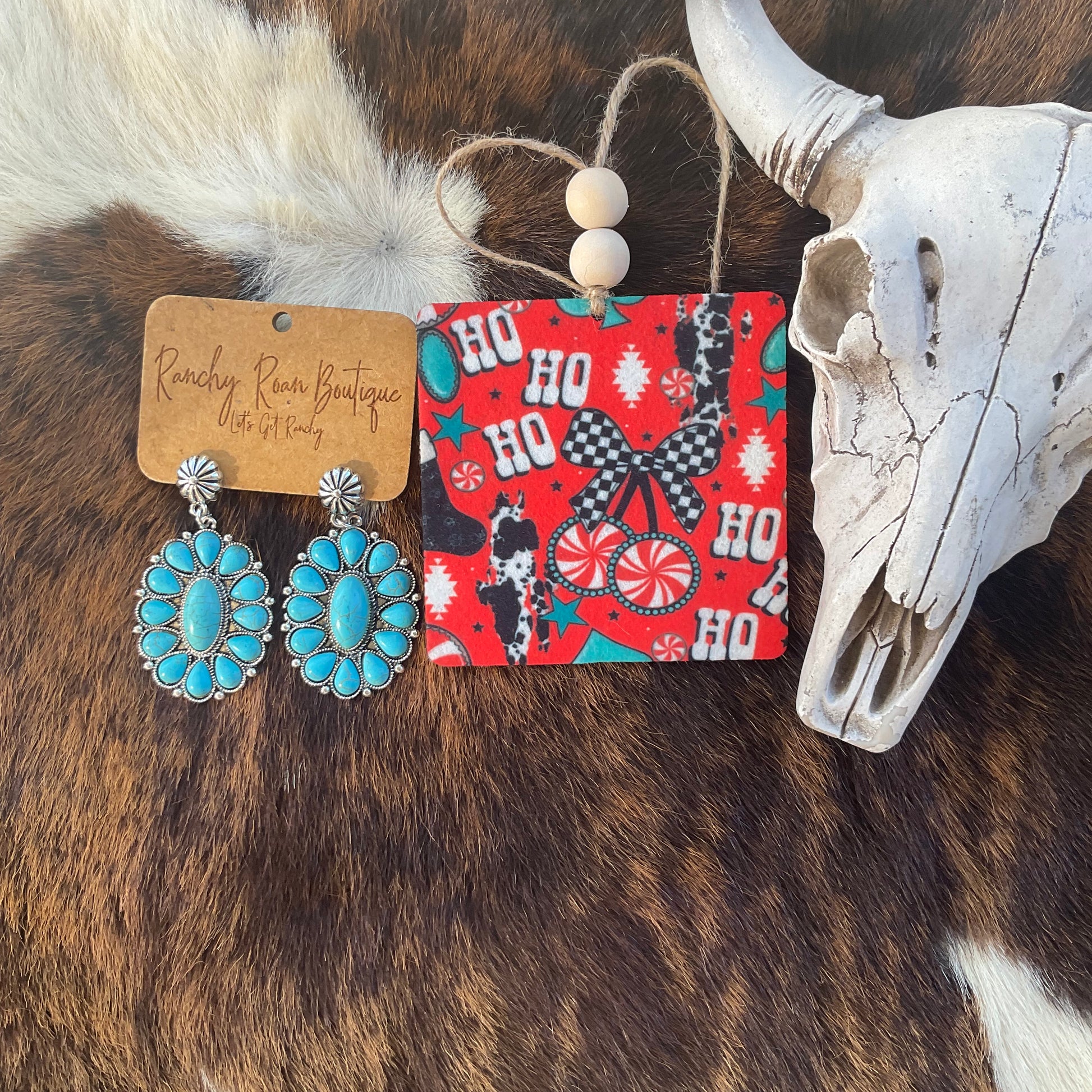 Ho Ho Ho Western Christmas Felt Freshie featuring red background with cowhide, peppermint, turquoise stars, and gingham bow beside turquoise earrings and skull décor.