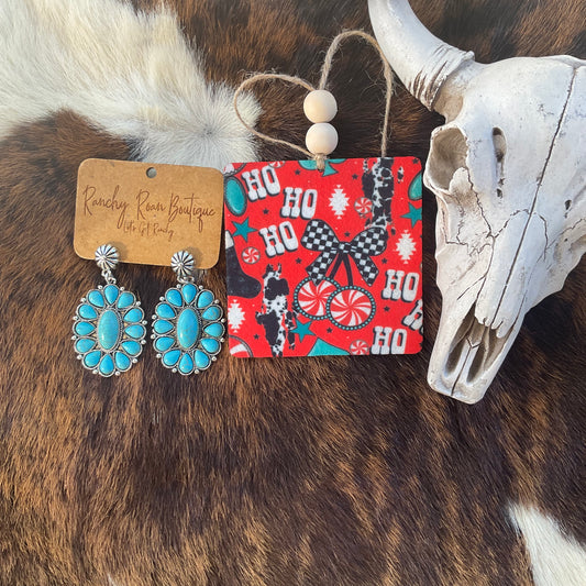 Ho Ho Ho Western Christmas Felt Freshie featuring red background with cowhide, peppermint, turquoise stars, and gingham bow beside turquoise earrings and skull décor.
