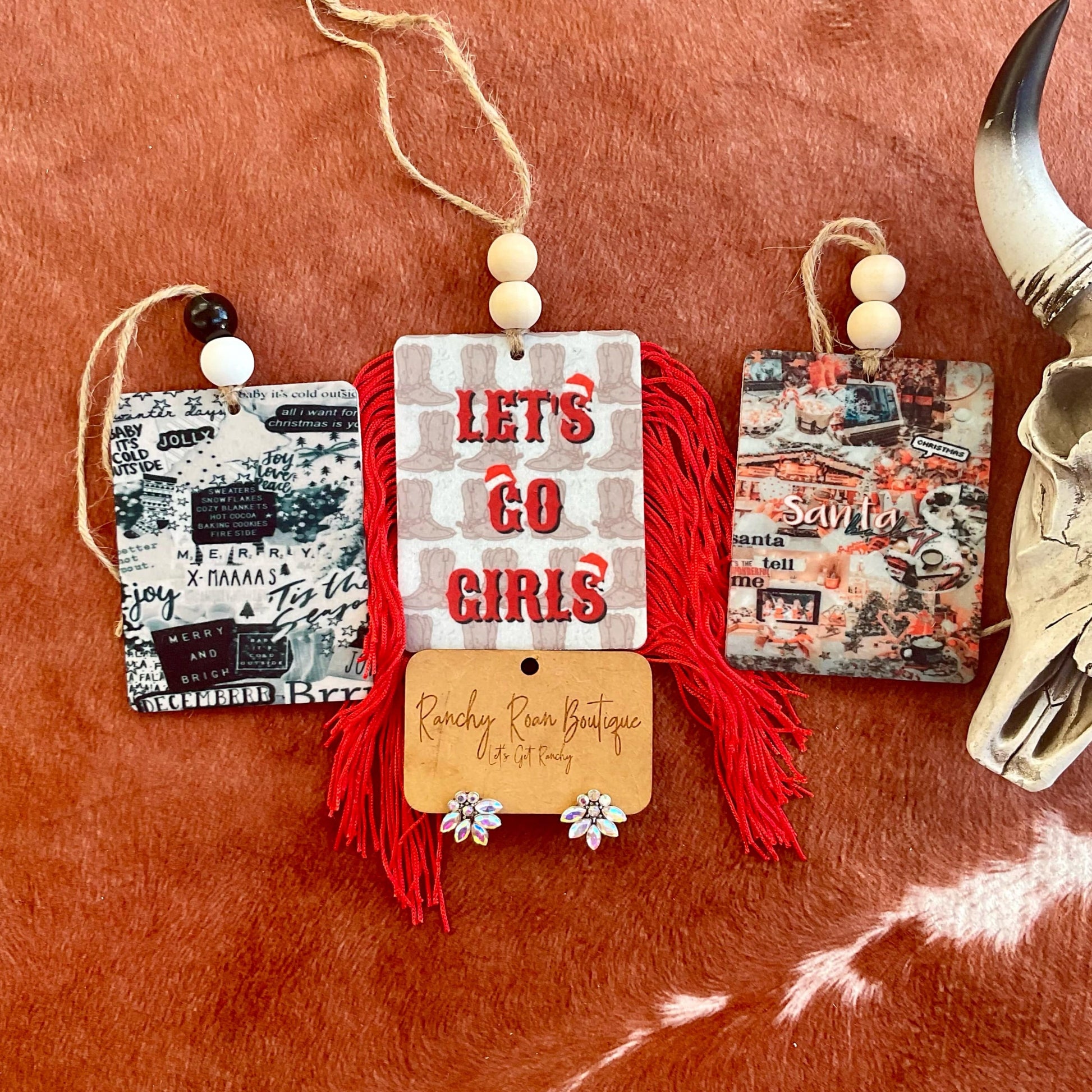 Holiday Western Double-Sided Felt Freshies featuring designs like “Let’s Go Girls” and “Santa,” displayed with colorful fringe and bead accents on a rustic background with a cow skull.