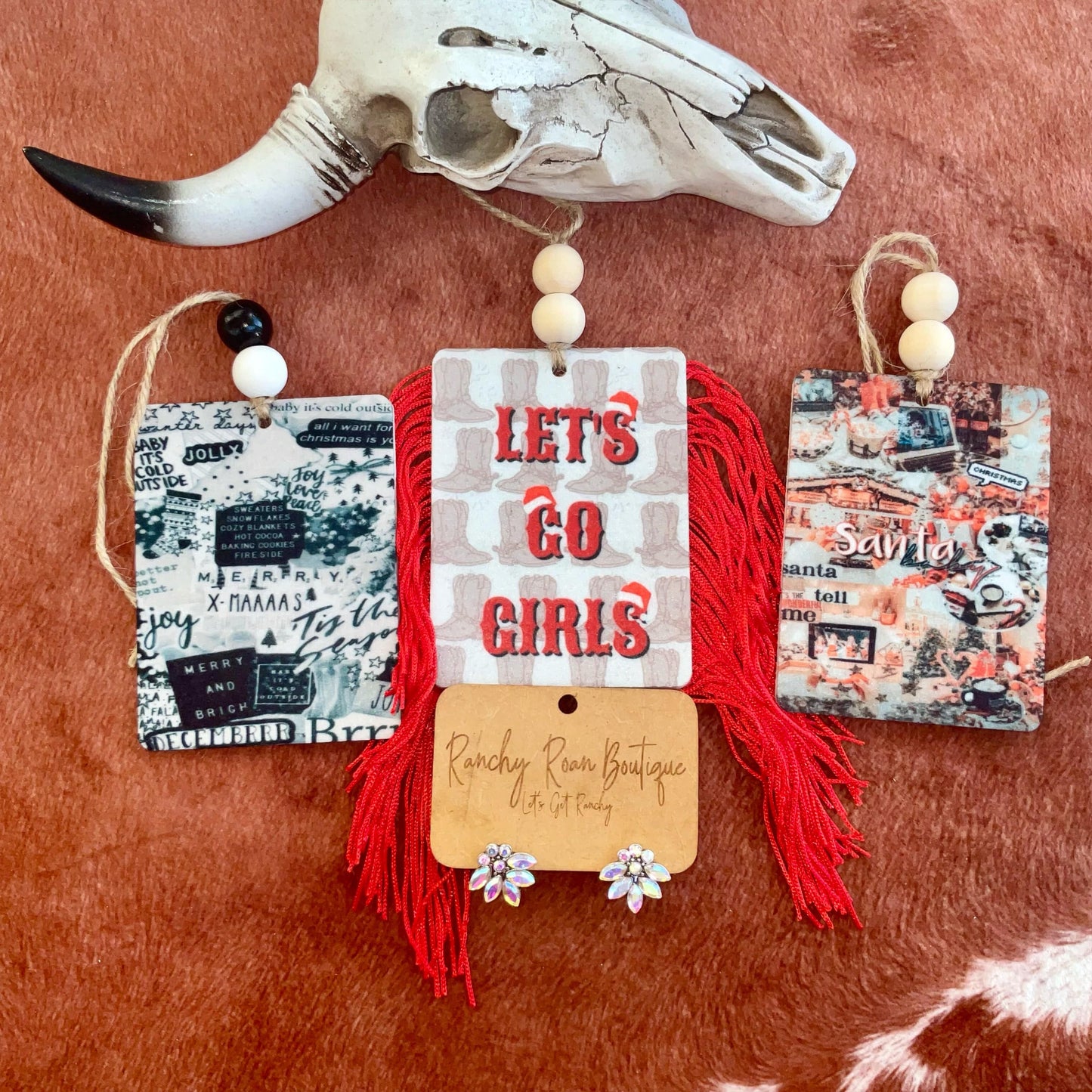 Holiday Western Double-Sided Felt Freshies featuring designs like “Let’s Go Girls” and “Santa,” displayed with colorful fringe and bead accents on a rustic background with a cow skull.