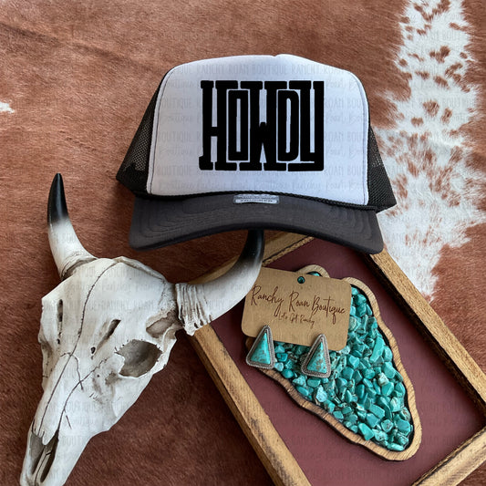 Retro Western trucker hat featuring a bold “Howdy” graphic, displayed with turquoise earrings and a decorative skull on a cowhide background.