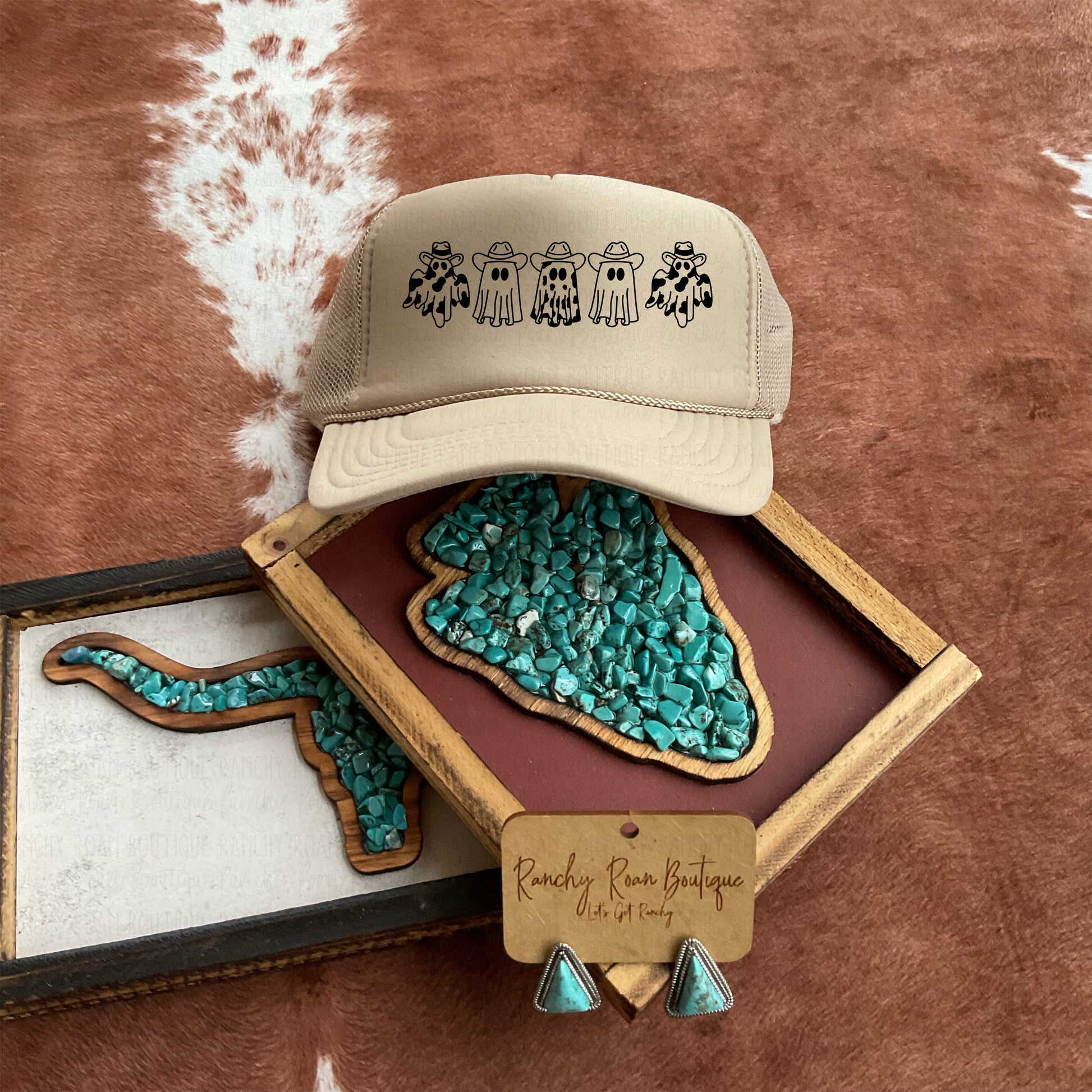 A neutral tan trucker hat from Ranchy Roan Boutique featuring a row of playful ghosts dressed in Western attire. Styled with turquoise decor, enhancing the Western theme.