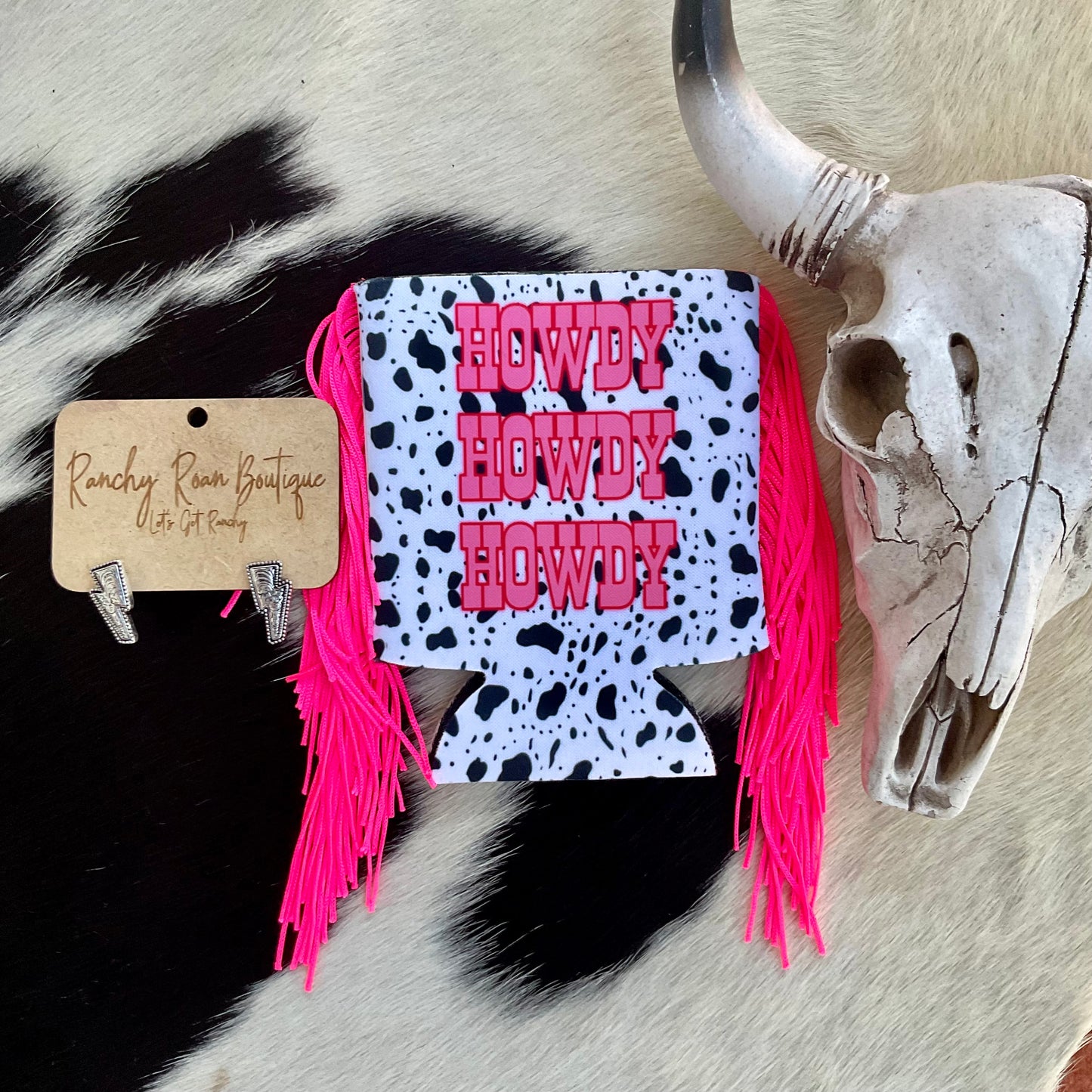 Close-up of the fringe cow print koozie, featuring bold pink text and fringe detail against a rustic background.