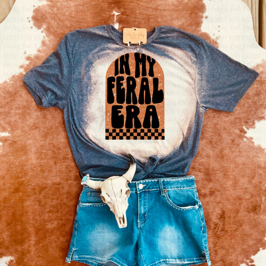In My Feral Era T-Shirt with Denim Shorts and Skull Decor: A graphic tee with a retro “In My Feral Era” design, displayed with denim shorts and a decorative skull on a cowhide rug.