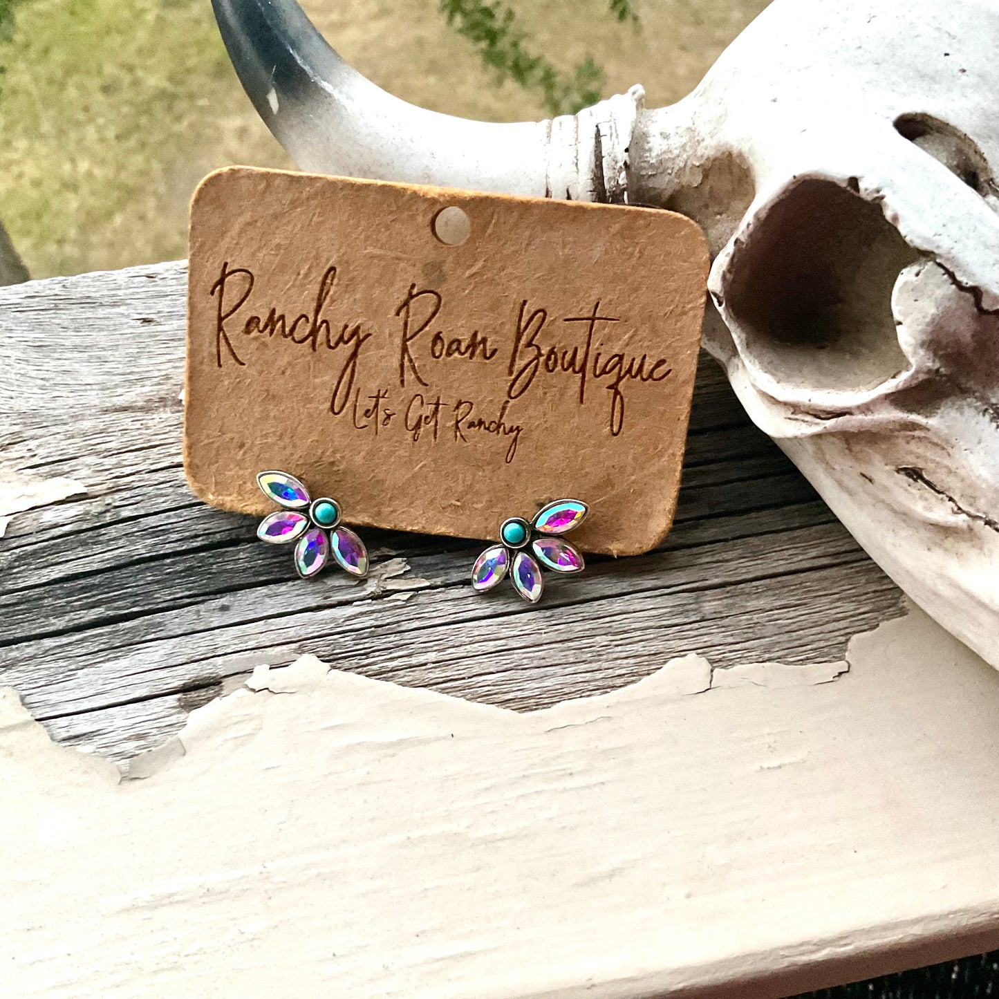 Iridescent floral earrings with turquoise center displayed in a small cactus-themed pot, showcasing their vibrant sparkle