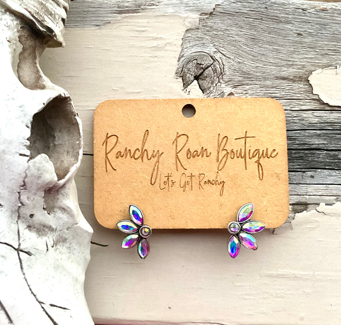 Iridescent floral stud earrings with petal-shaped stones, displayed on Ranchy Roan Boutique card, styled next to a Western skull decor.