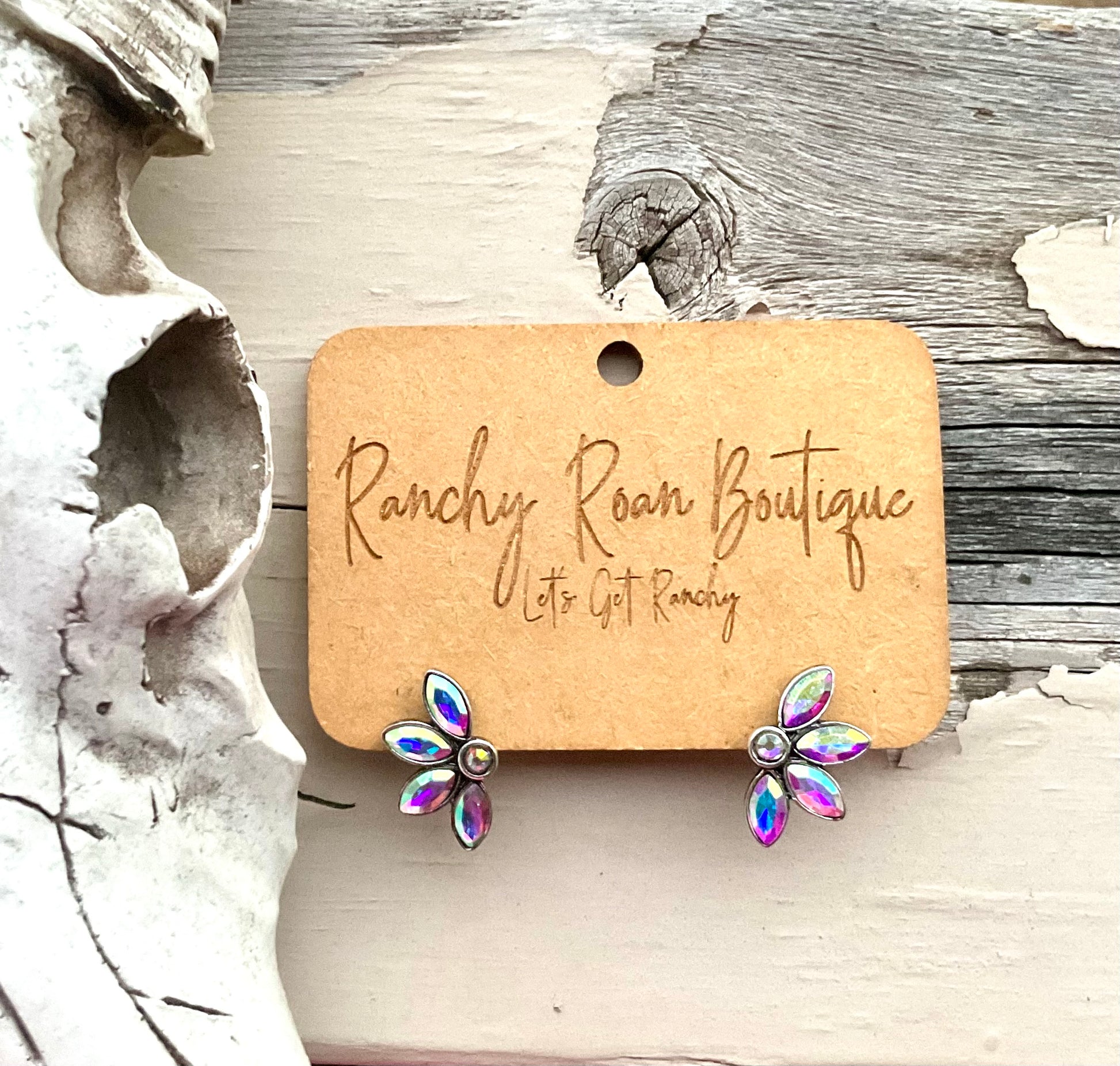 Iridescent floral stud earrings with petal-shaped stones, displayed on Ranchy Roan Boutique card, styled next to a Western skull decor.