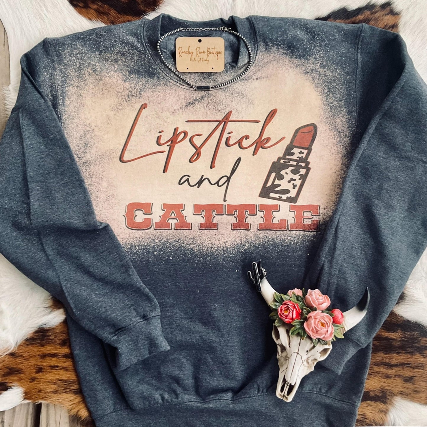 Lipstick and Cattle Western Graphic Sweatshirt featuring bold text and a lipstick icon on a bleached background, styled with rustic Western accessories.