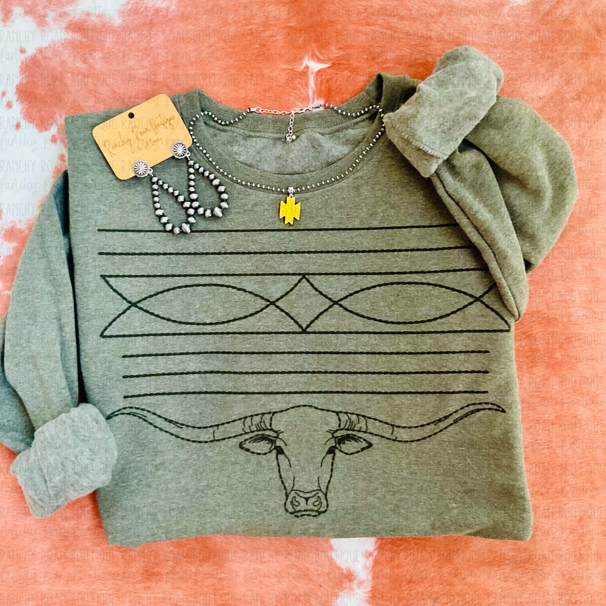 Folded Western Longhorn Boot Stitch Sweatshirt styled with accessories and displayed on a cowhide rug.