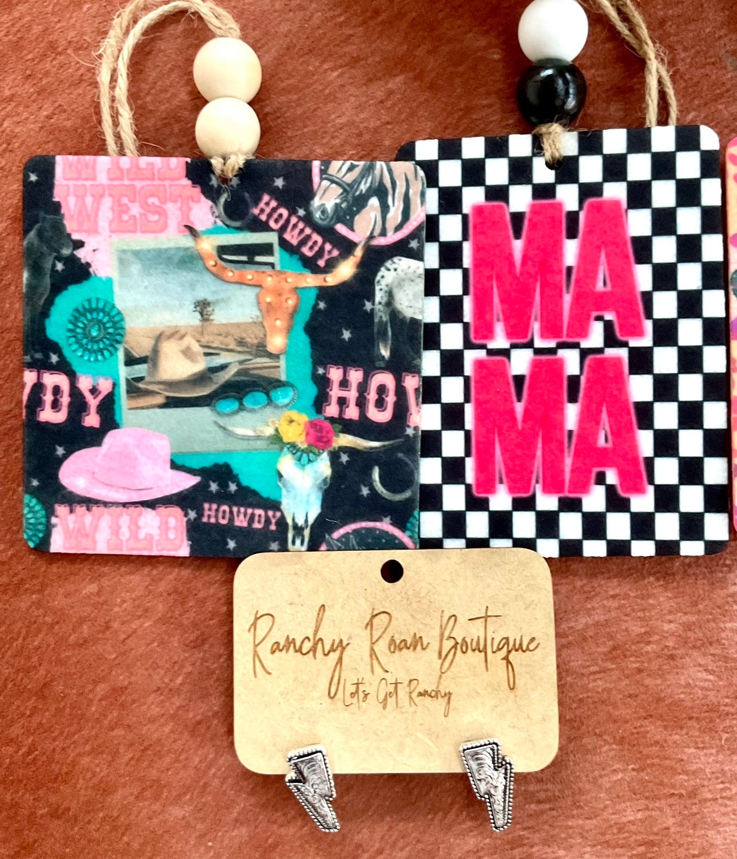  Checkered “Mama” felt air freshener in bold pink and black, styled with Western decor on a rustic surface.
