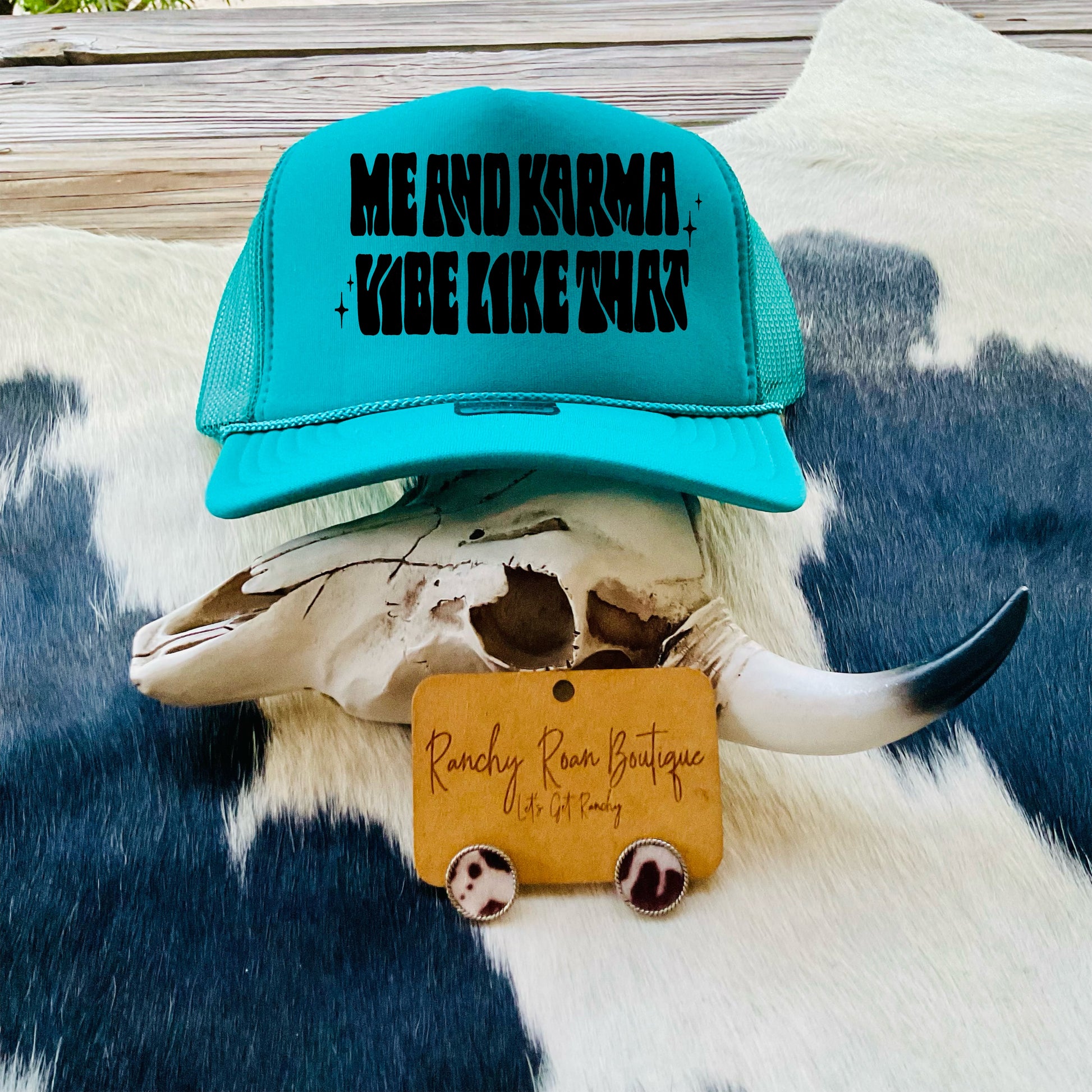  Vibrant turquoise trucker hat with bold black text displayed on a Western skull and cowhide background.
