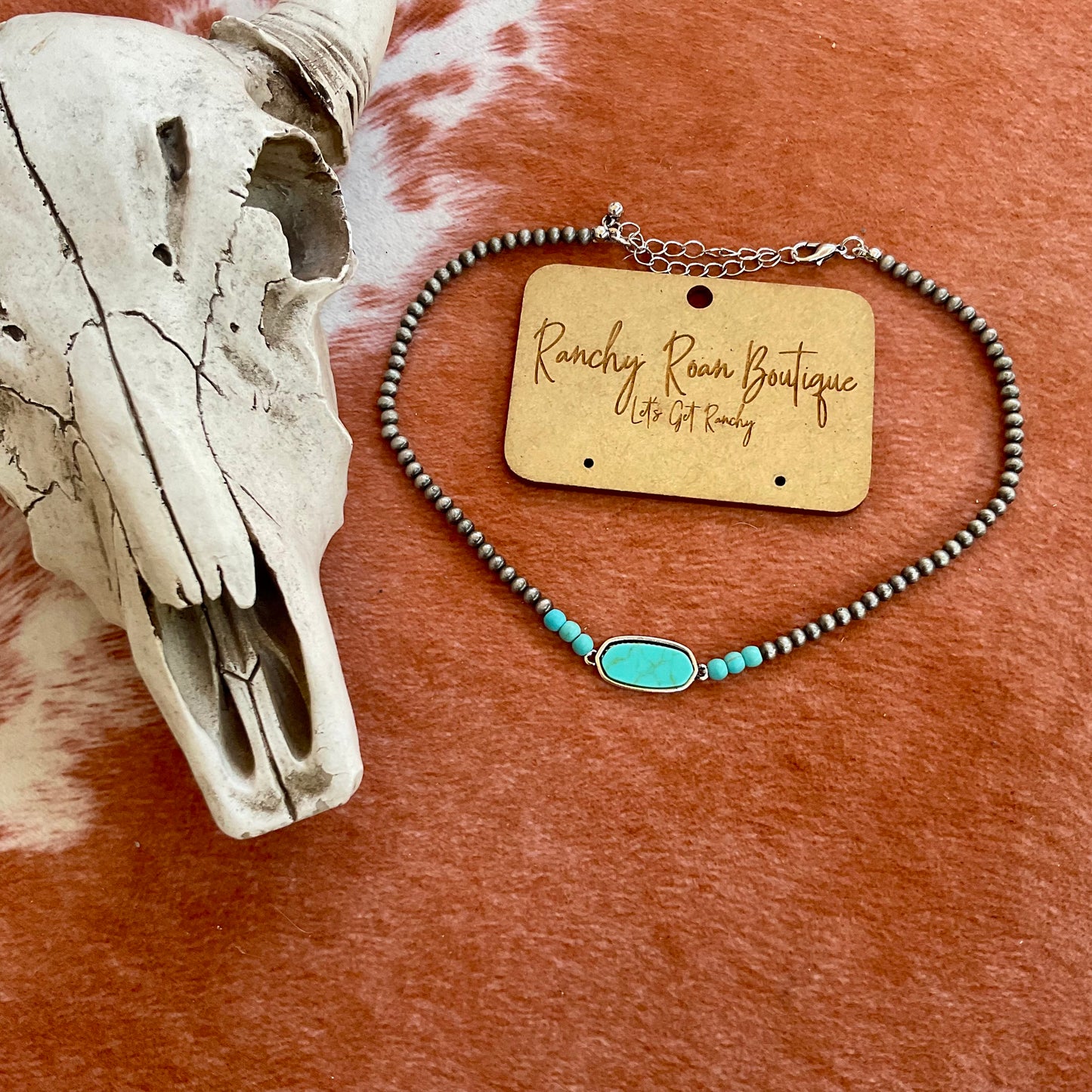 Close-up of a Navajo-style beaded choker with a turquoise stone accent, shown on a rustic background with cow skull decor.