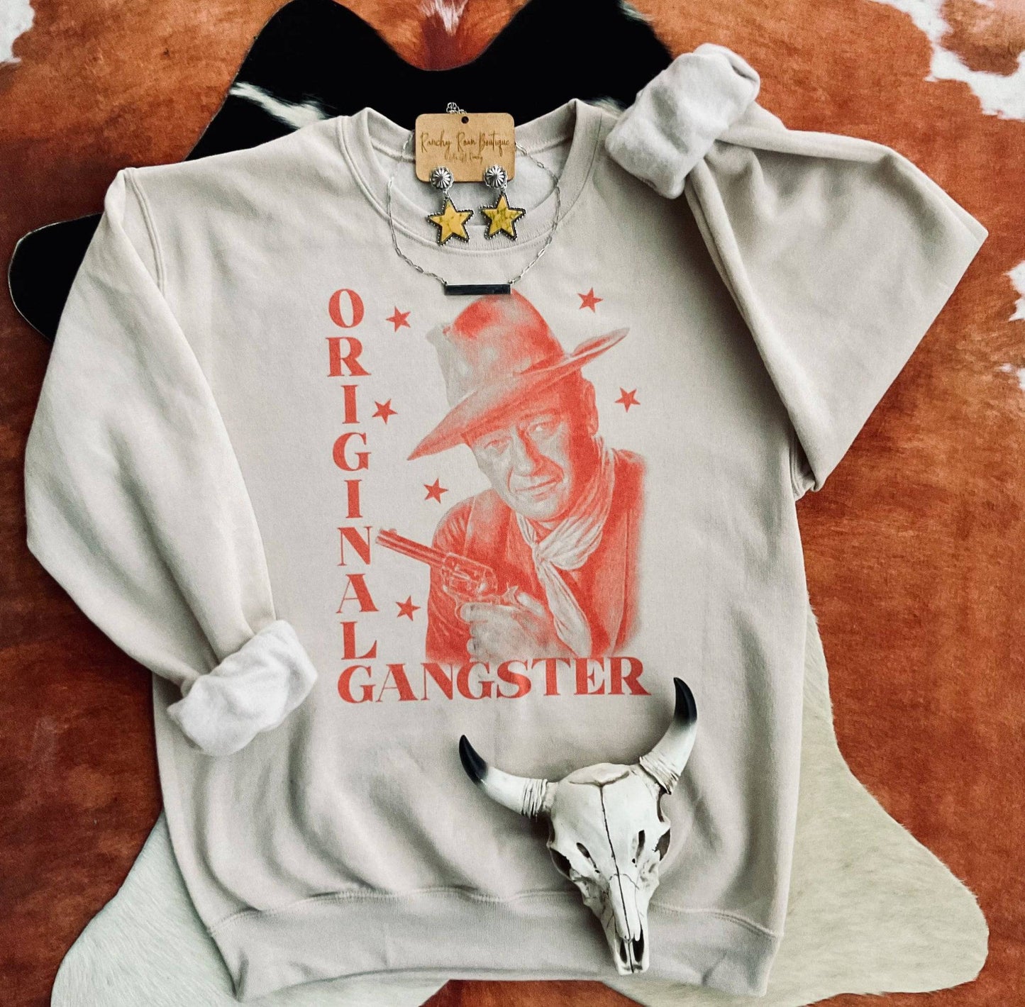 Original Gangster Western Graphic Sweatshirt featuring a vintage cowboy graphic with bold red text on a soft, beige background, styled with rustic Western accessories.