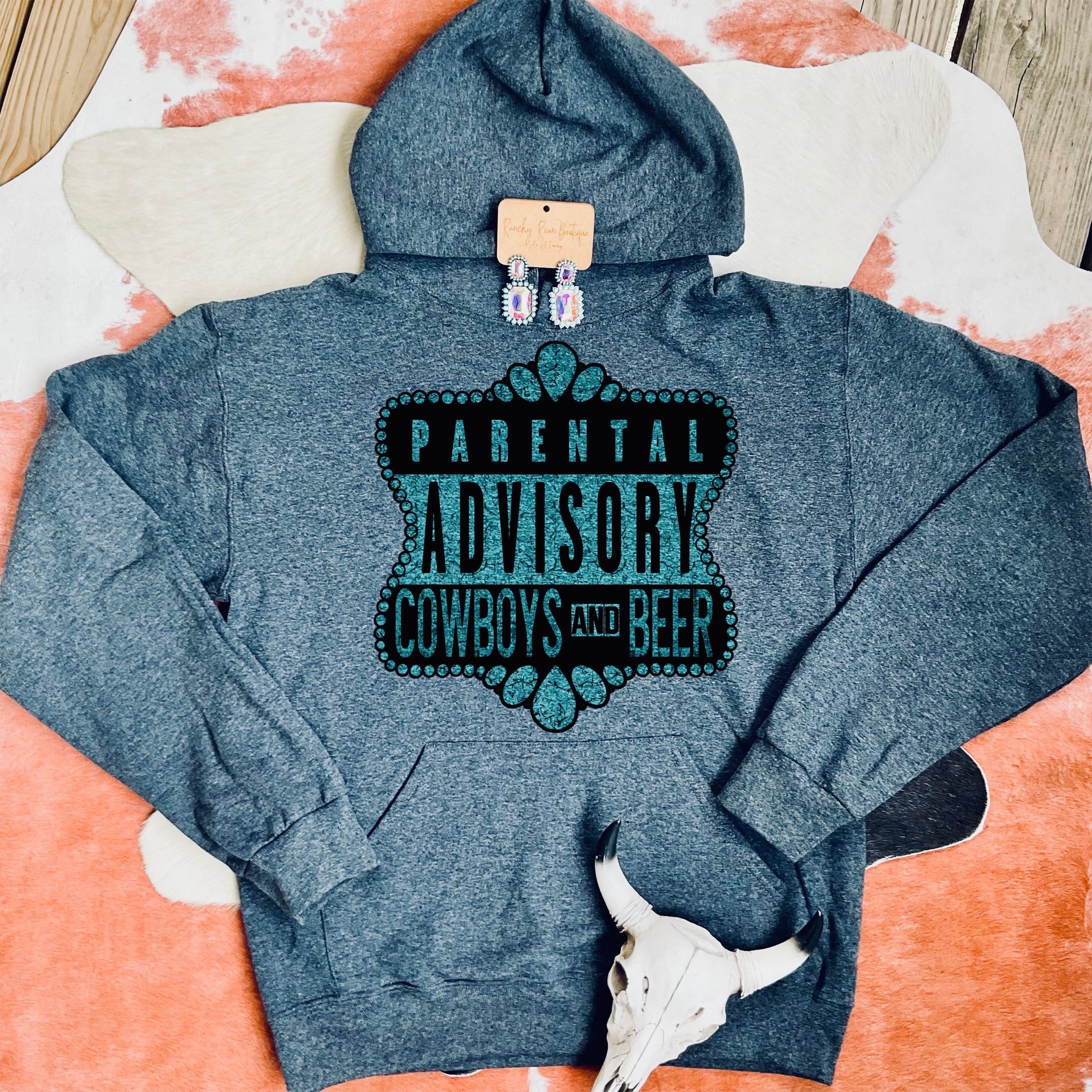 Comfortable unisex hoodie in a heather gray color featuring the bold “Parental Advisory: Cowboys and Beer” design in teal lettering, styled with Western accents.