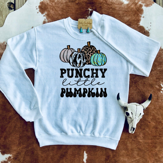 Punchy Little Pumpkin Graphic Sweatshirt with Skull Decor.White graphic sweatshirt featuring bold patterned pumpkins and “Punchy Little Pumpkin” text, displayed with turquoise earrings and a decorative skull on a cowhide background.
