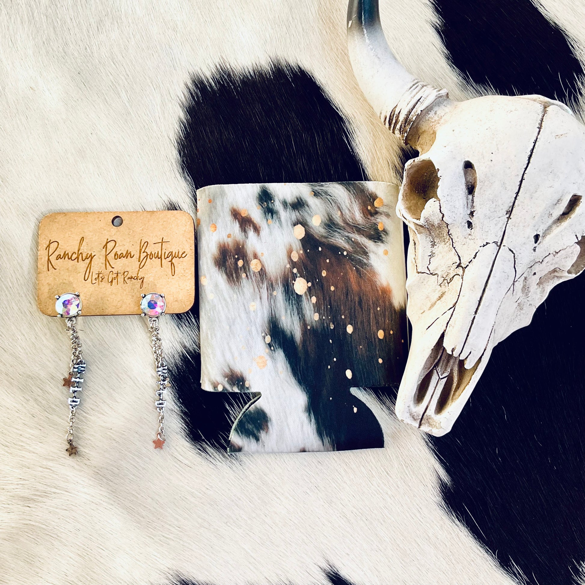 Regular-sized can koozie with a cowhide pattern and gold splatters, displayed on a cowhide background next to Western decor.