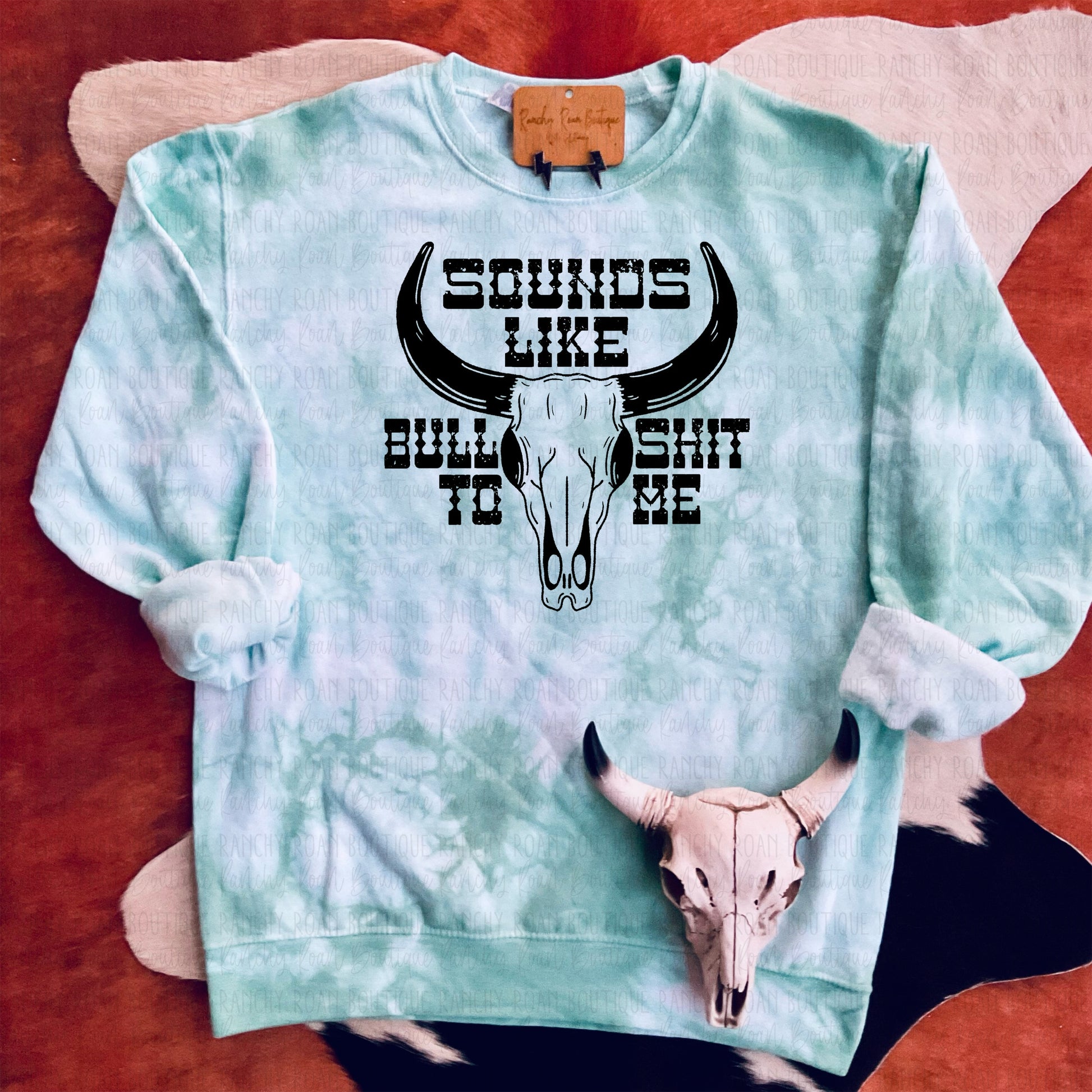 Turquoise tie-dye sweatshirt featuring “Sounds Like Bull to Me” text with a bull skull graphic.