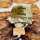 Tattoos Are Trashy Camo Trucker Hat featuring bold black text on an olive green background with camo accents, styled on a rustic Western backdrop